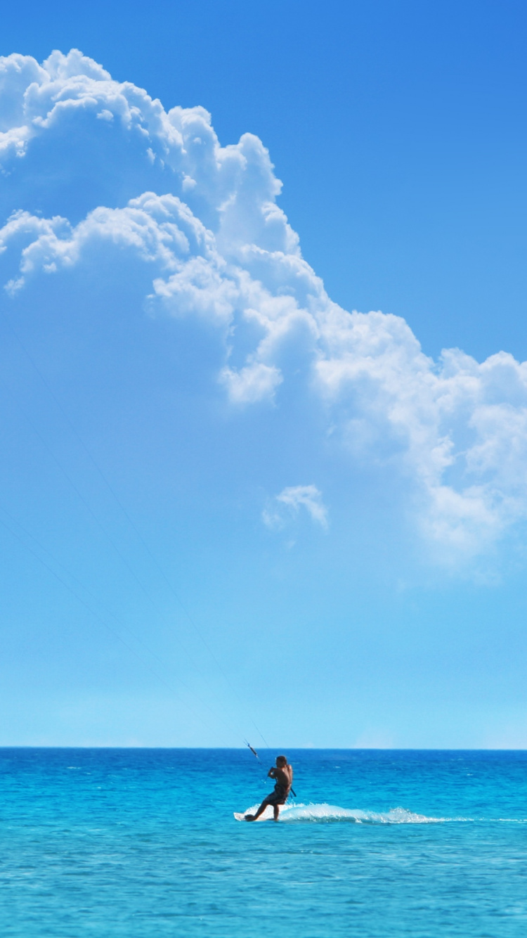 Mann in Blauen Shorts, Der Tagsüber Blaue Und Schwarze Kitesurfen Auf Dem Meer Hält. Wallpaper in 750x1334 Resolution