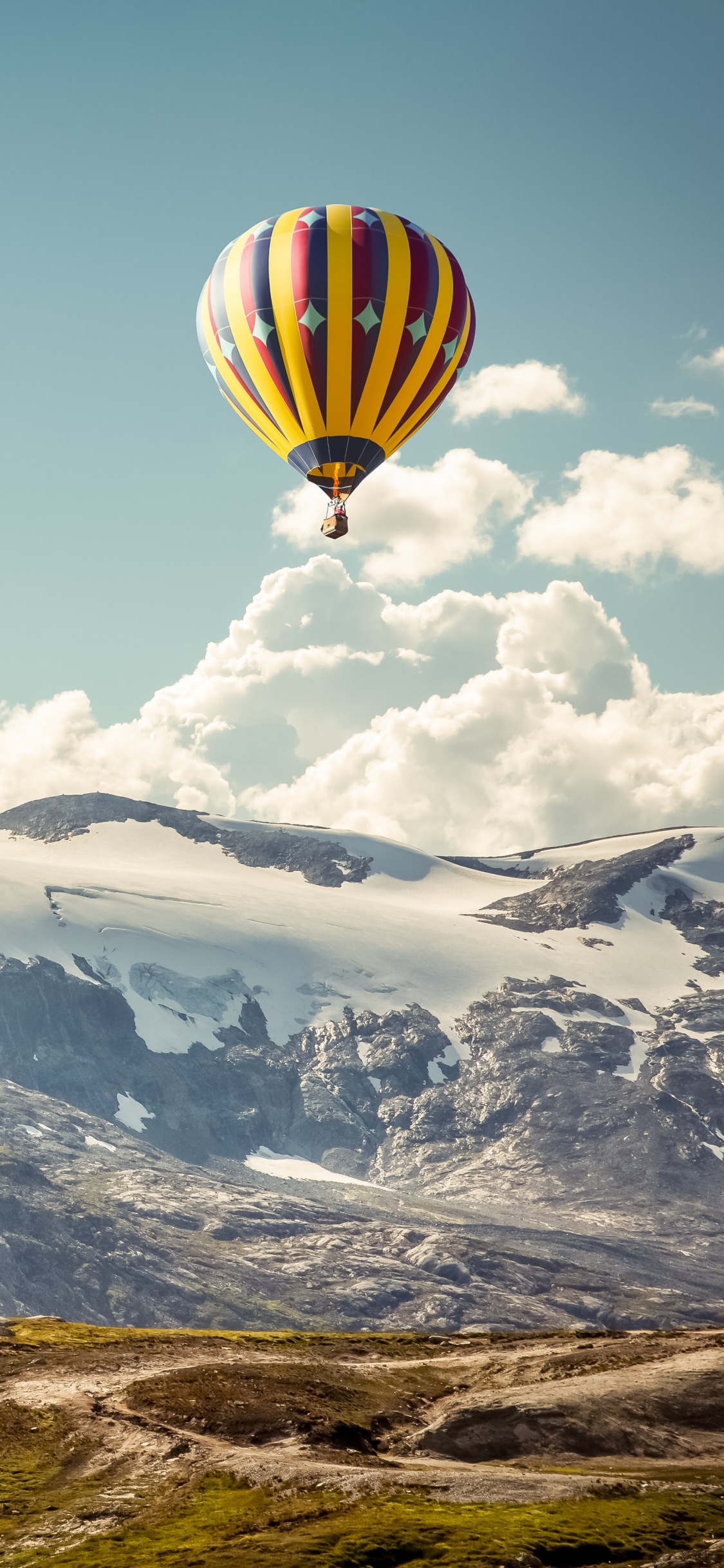 Gelber Und Grüner Heißluftballon, Der Tagsüber Über Schneebedeckte Berge Fliegt. Wallpaper in 1125x2436 Resolution