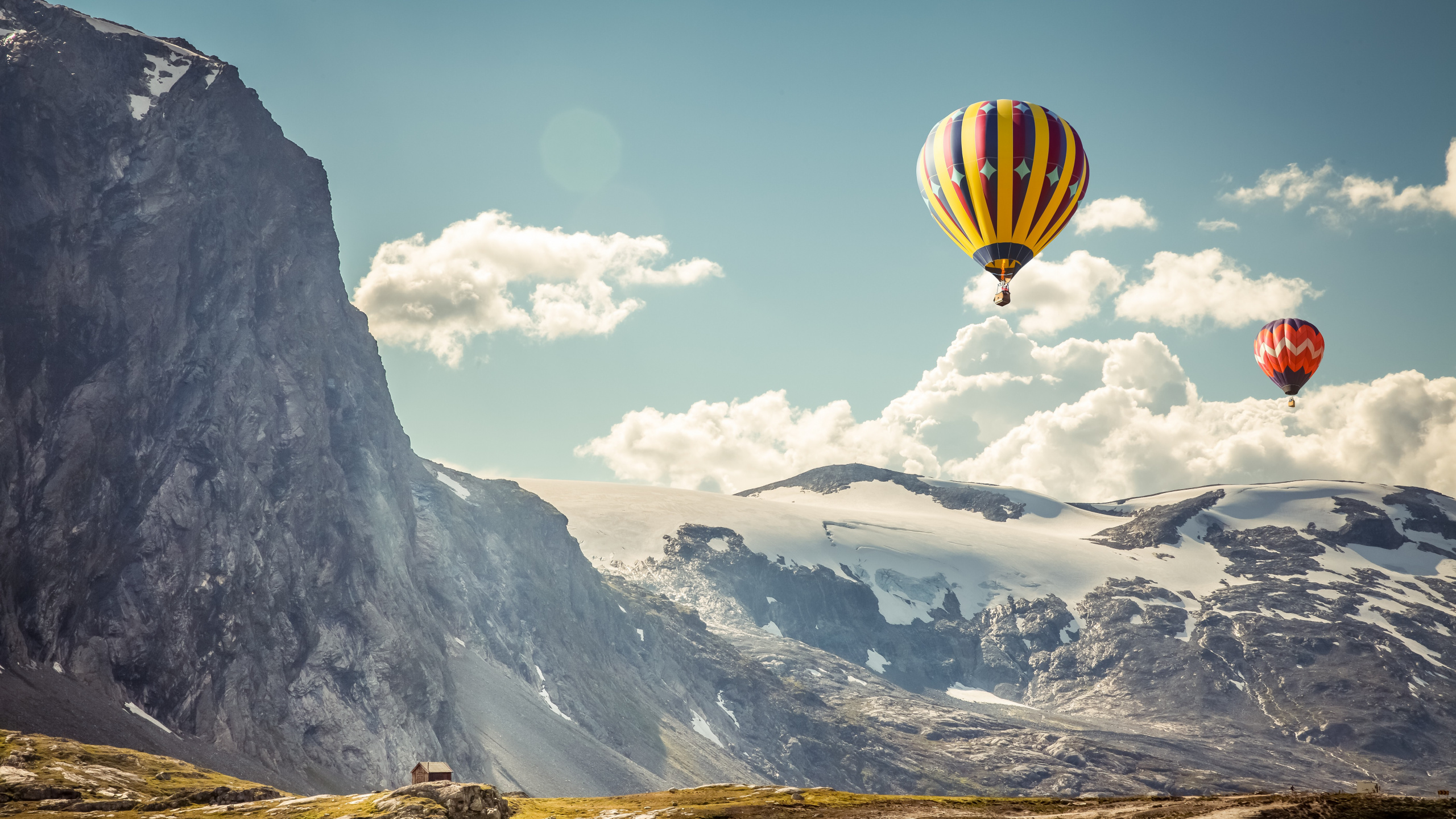 Gelber Und Grüner Heißluftballon, Der Tagsüber Über Schneebedeckte Berge Fliegt. Wallpaper in 2560x1440 Resolution