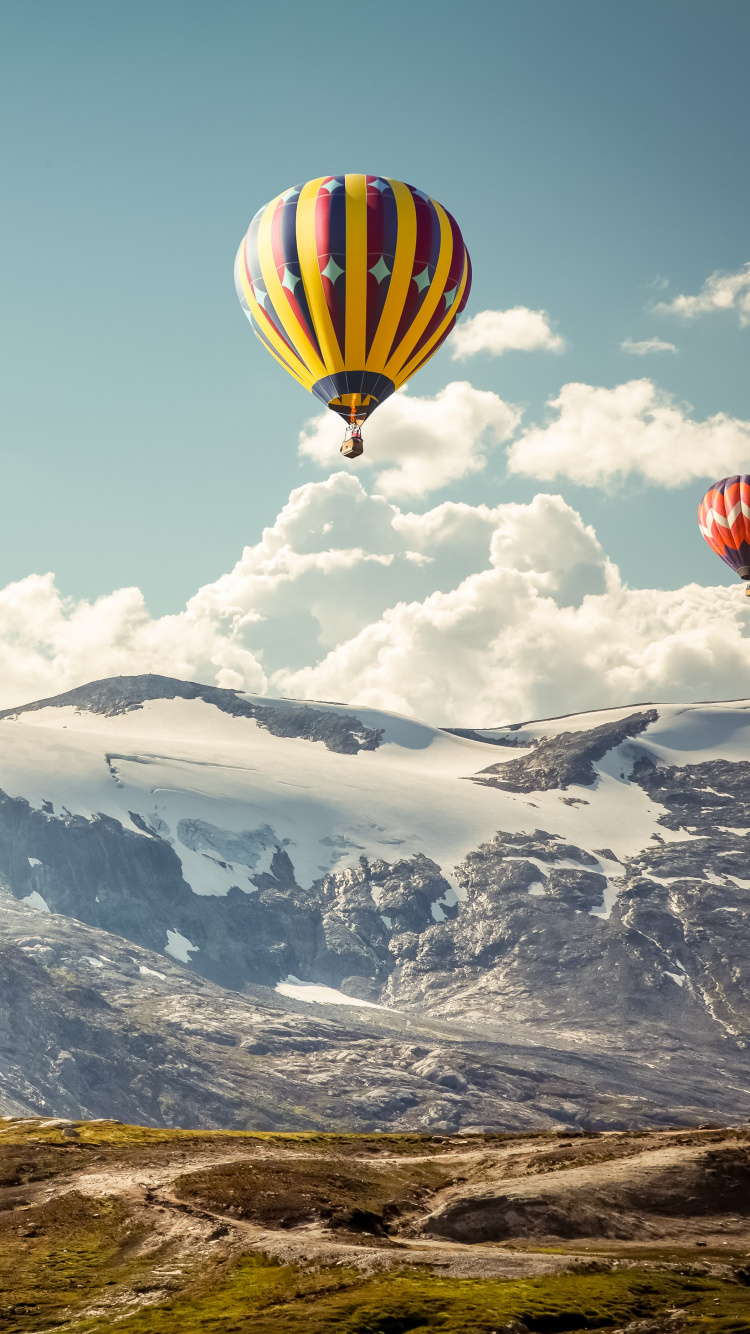 Gelber Und Grüner Heißluftballon, Der Tagsüber Über Schneebedeckte Berge Fliegt. Wallpaper in 750x1334 Resolution