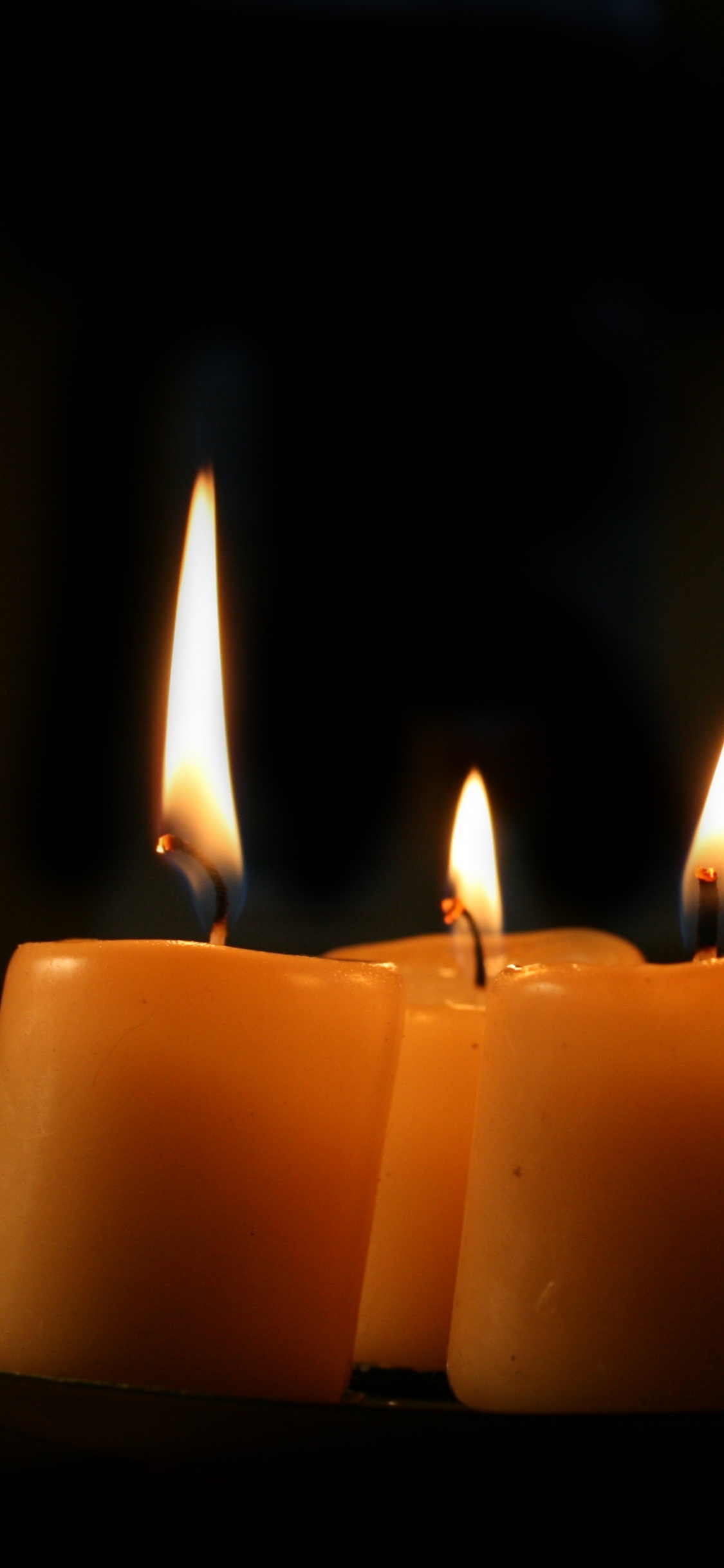 3 Lighted Candles on Black Background. Wallpaper in 1125x2436 Resolution