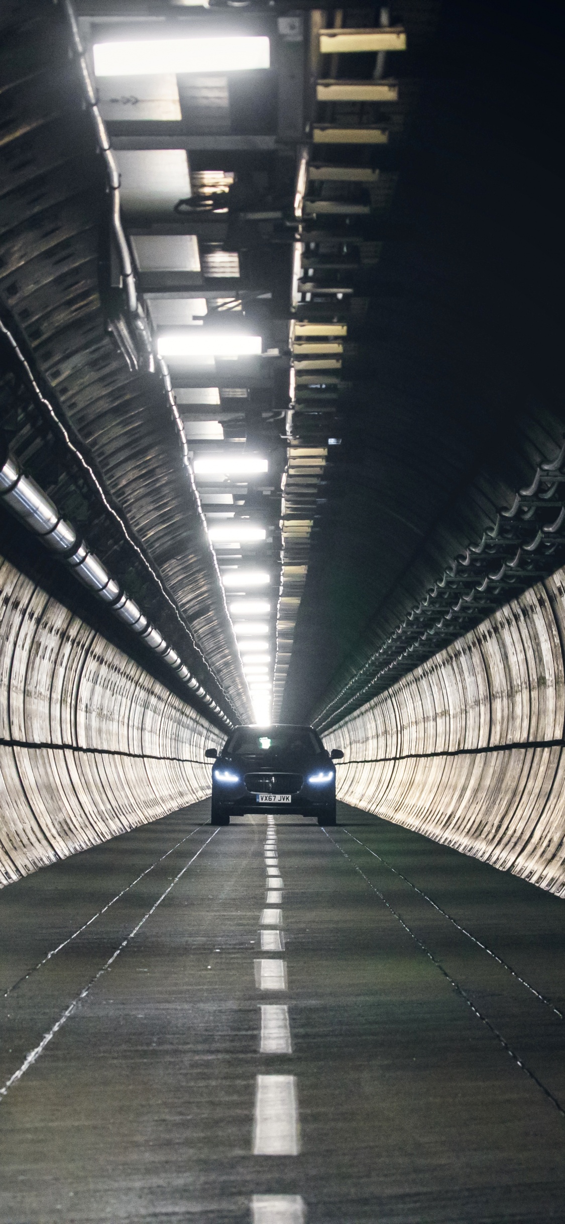 Hombre de Chaqueta Negra Caminando Sobre el Túnel. Wallpaper in 1125x2436 Resolution