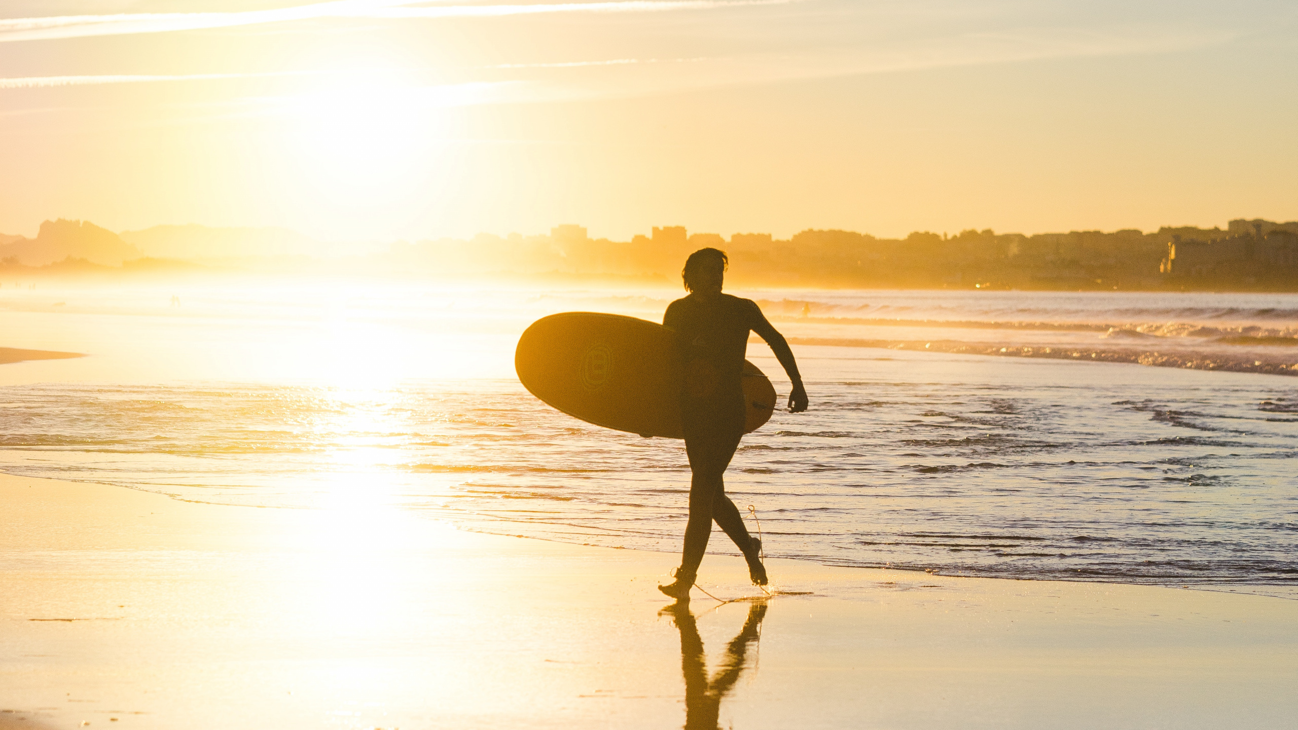 Hombre en Shorts Negros Sosteniendo la Tabla de Surf Caminando Por la Orilla Del Mar Durante la Puesta de Sol. Wallpaper in 2560x1440 Resolution