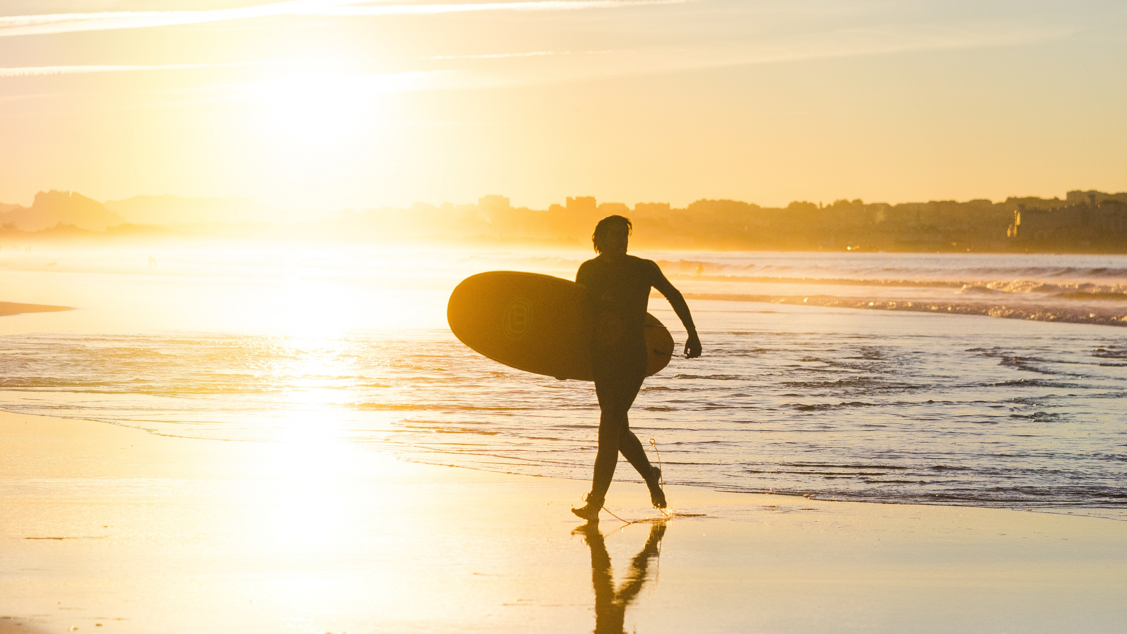 Hombre en Shorts Negros Sosteniendo la Tabla de Surf Caminando Por la Orilla Del Mar Durante la Puesta de Sol. Wallpaper in 3840x2160 Resolution