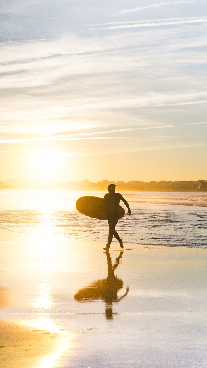 Mann in Schwarzen Shorts Mit Surfbrett, Der Während Des Sonnenuntergangs am Meer Spazieren Geht. Wallpaper in 720x1280 Resolution