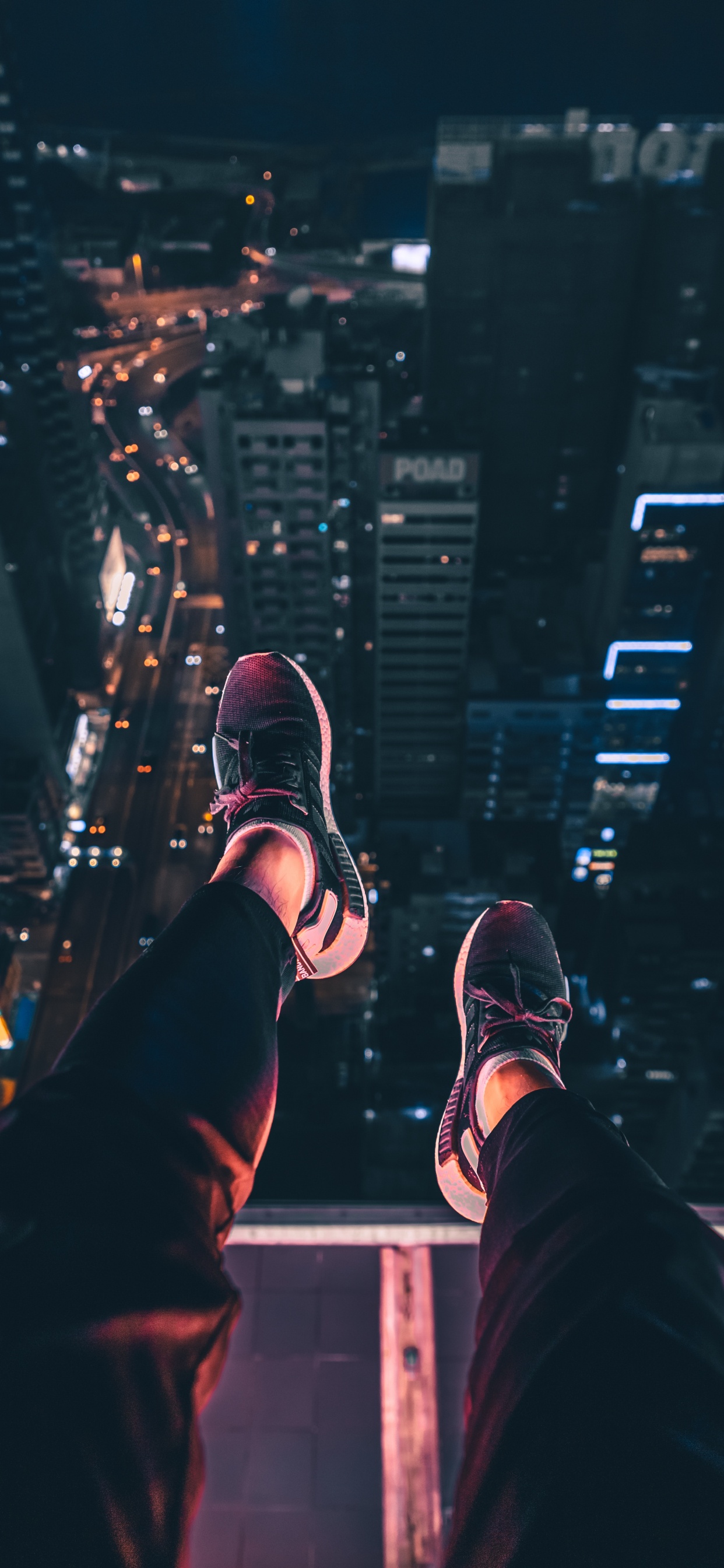 Persona Con Pantalones Negros y Zapatillas Blancas y Negras Sentada en el Edificio Durante la Noche. Wallpaper in 1242x2688 Resolution