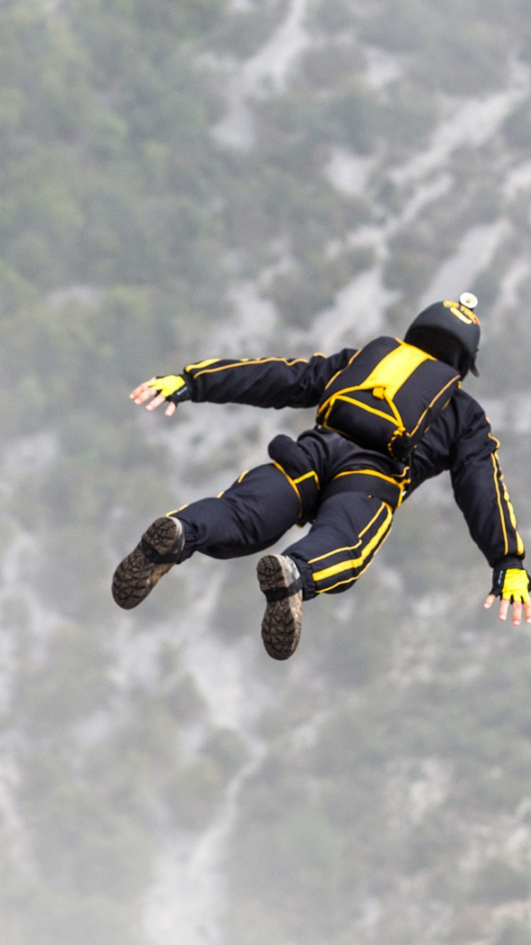 Homme en Veste Noire et Jaune et Pantalon Noir Sautant Dans Les Airs Sous Des Nuages Blancs. Wallpaper in 750x1334 Resolution