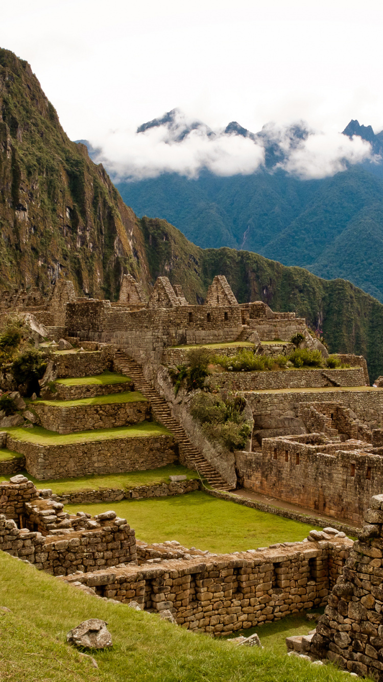 Braunes Betongebäude Auf Grünem Grasfeld in Der Nähe Des Berges Unter Weißen Wolken Tagsüber. Wallpaper in 750x1334 Resolution