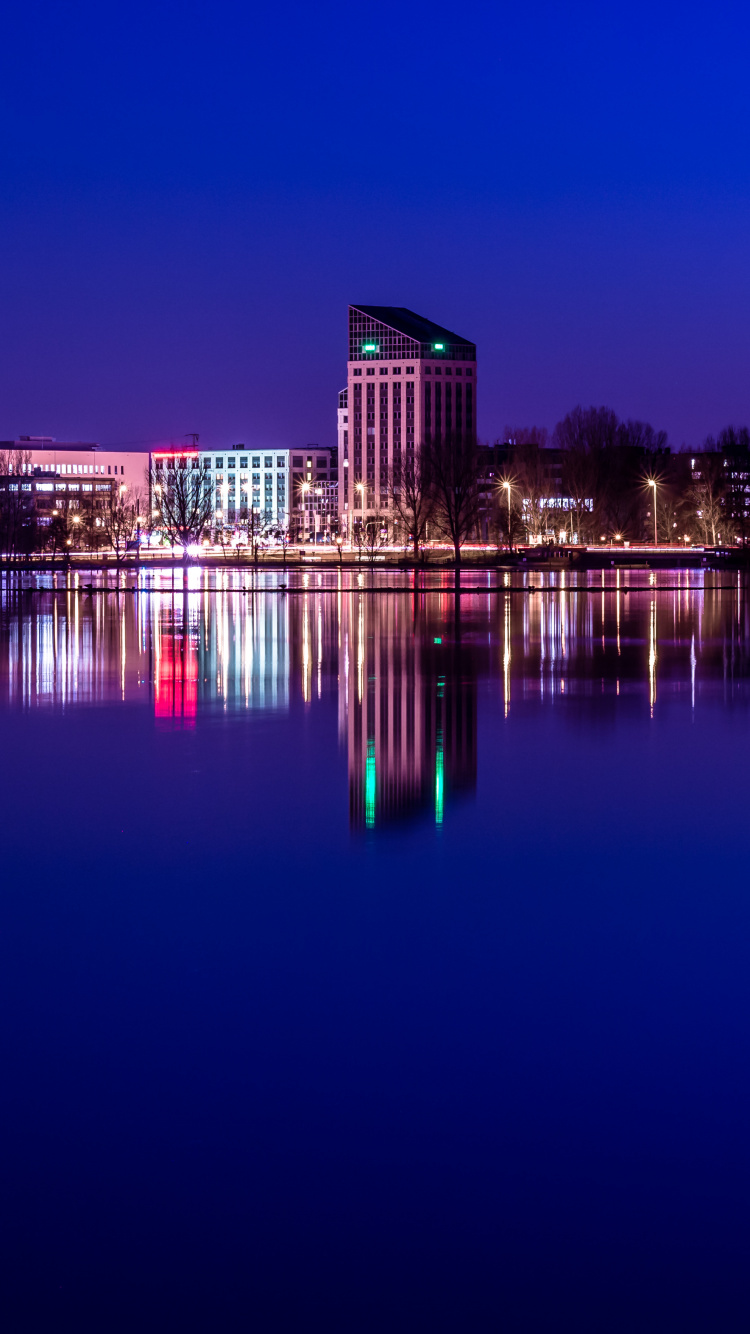 Brown Concrete Building Near Body of Water During Night Time. Wallpaper in 750x1334 Resolution