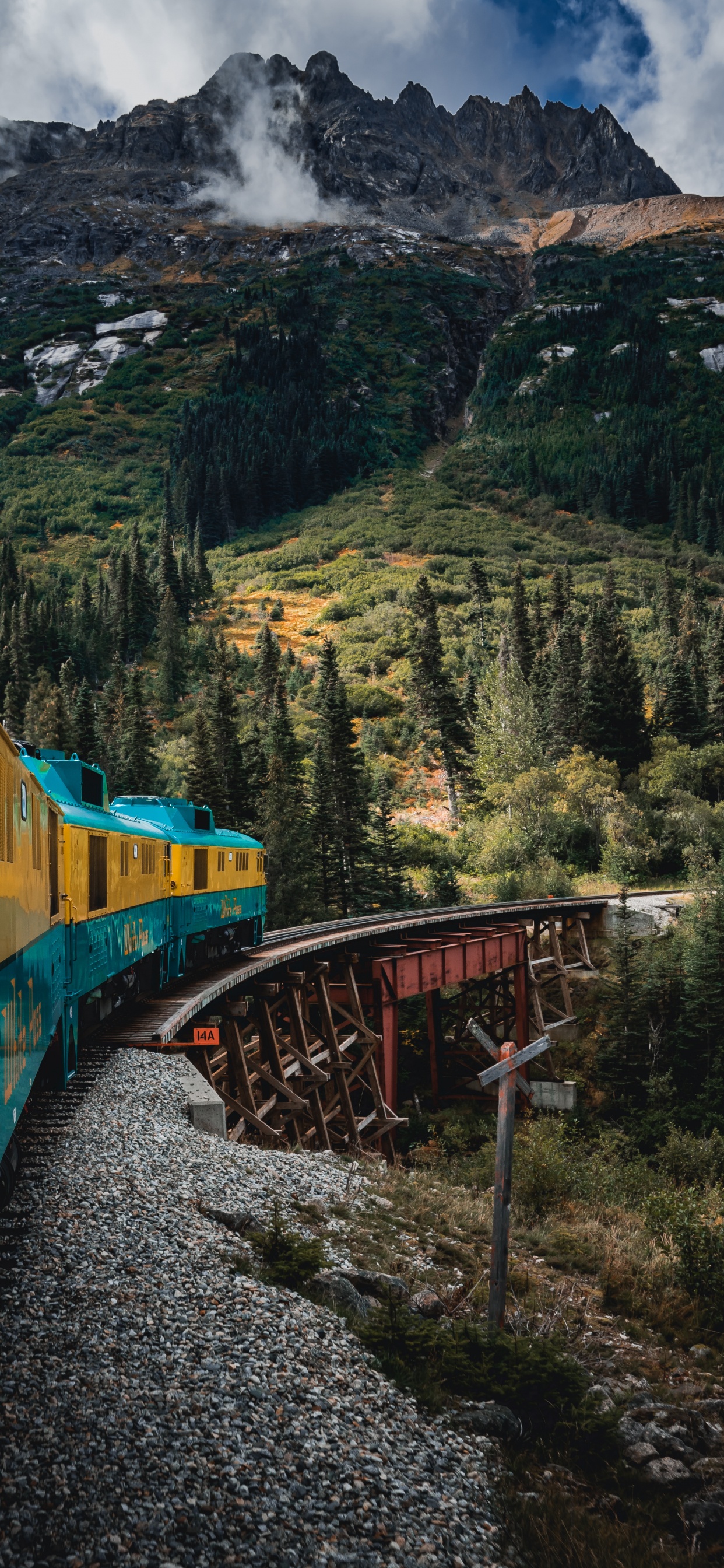 Yellow and Blue Train on Rail Tracks Near Green Trees and Mountain During Daytime. Wallpaper in 1242x2688 Resolution