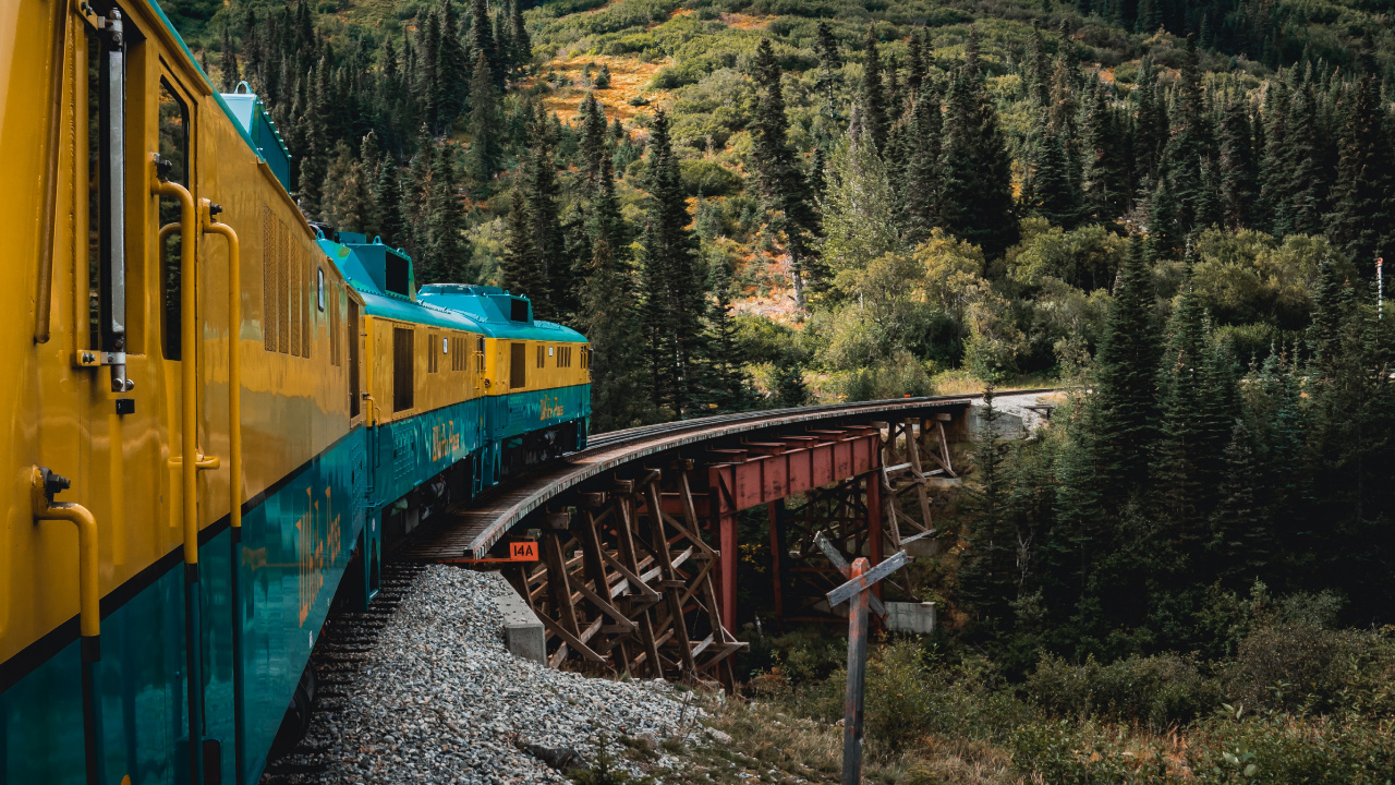 Yellow and Blue Train on Rail Tracks Near Green Trees and Mountain During Daytime. Wallpaper in 1280x720 Resolution