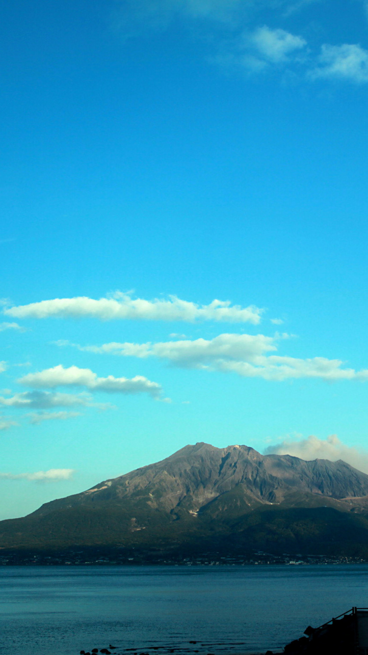 Montaña Verde Cerca Del Cuerpo de Agua Bajo un Cielo Azul Durante el Día. Wallpaper in 750x1334 Resolution