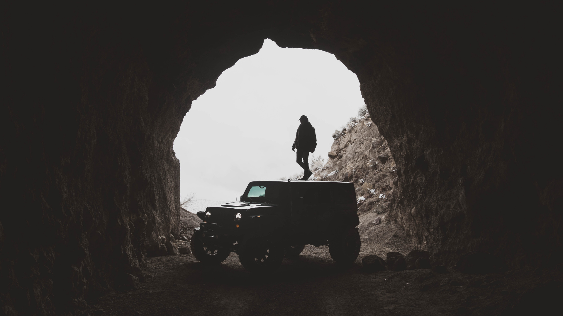 Man in Black Jacket Standing on Black Jeep Wrangler Inside Cave During Daytime. Wallpaper in 1920x1080 Resolution