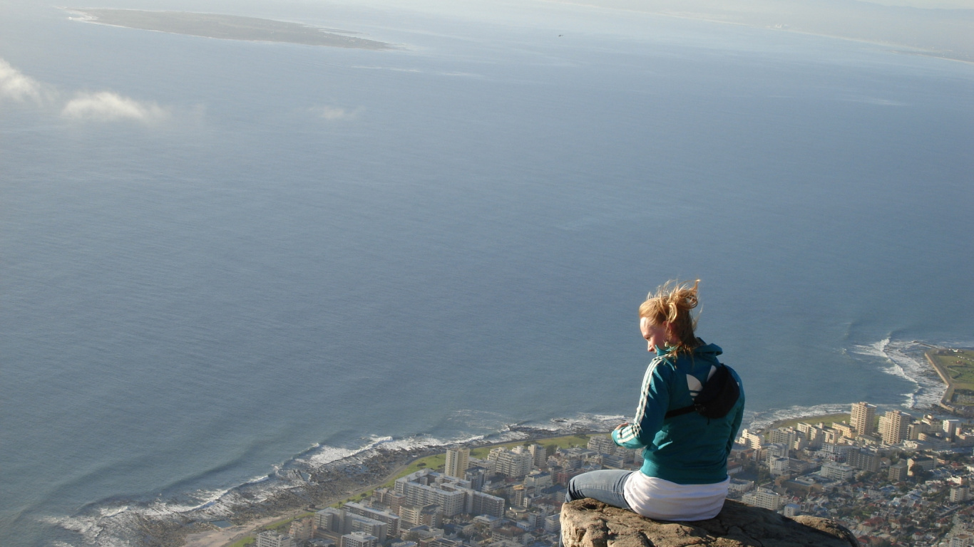 Woman in Blue Long Sleeve Shirt Sitting on Rock Formation Near Sea During Daytime. Wallpaper in 1366x768 Resolution