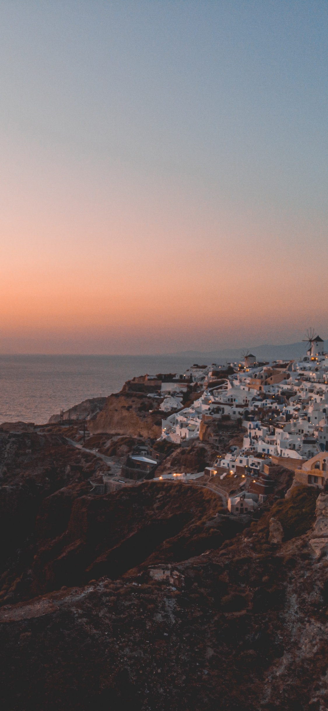 Brown Rocky Mountain Beside Sea During Sunset. Wallpaper in 1125x2436 Resolution