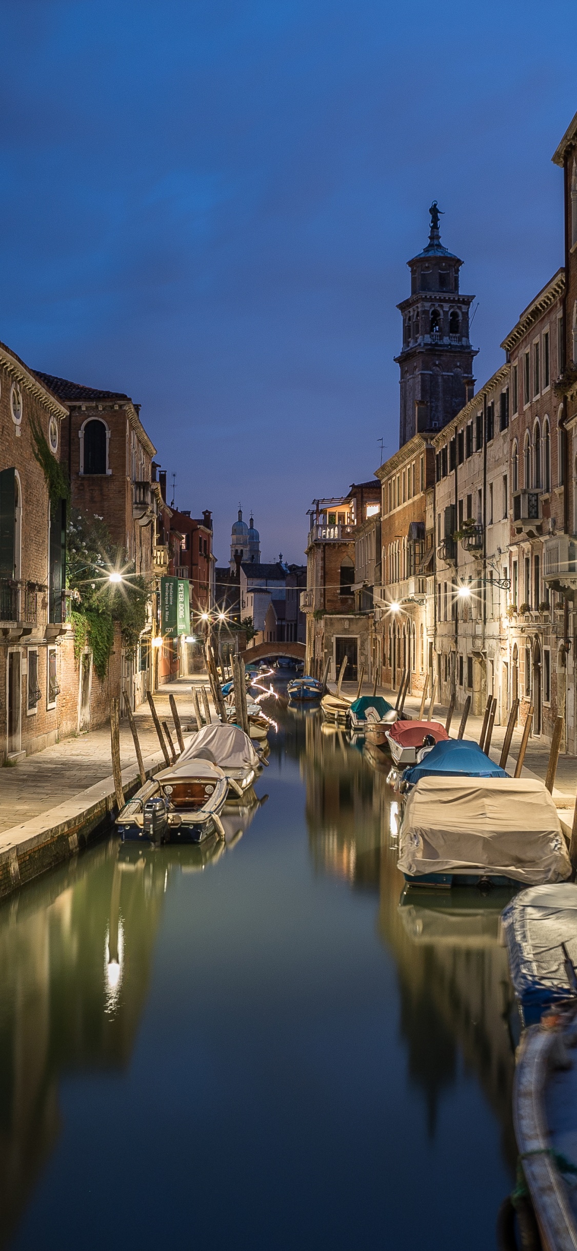 Blaues Boot Auf Dem Fluss Zwischen Den Gebäuden Tagsüber. Wallpaper in 1125x2436 Resolution