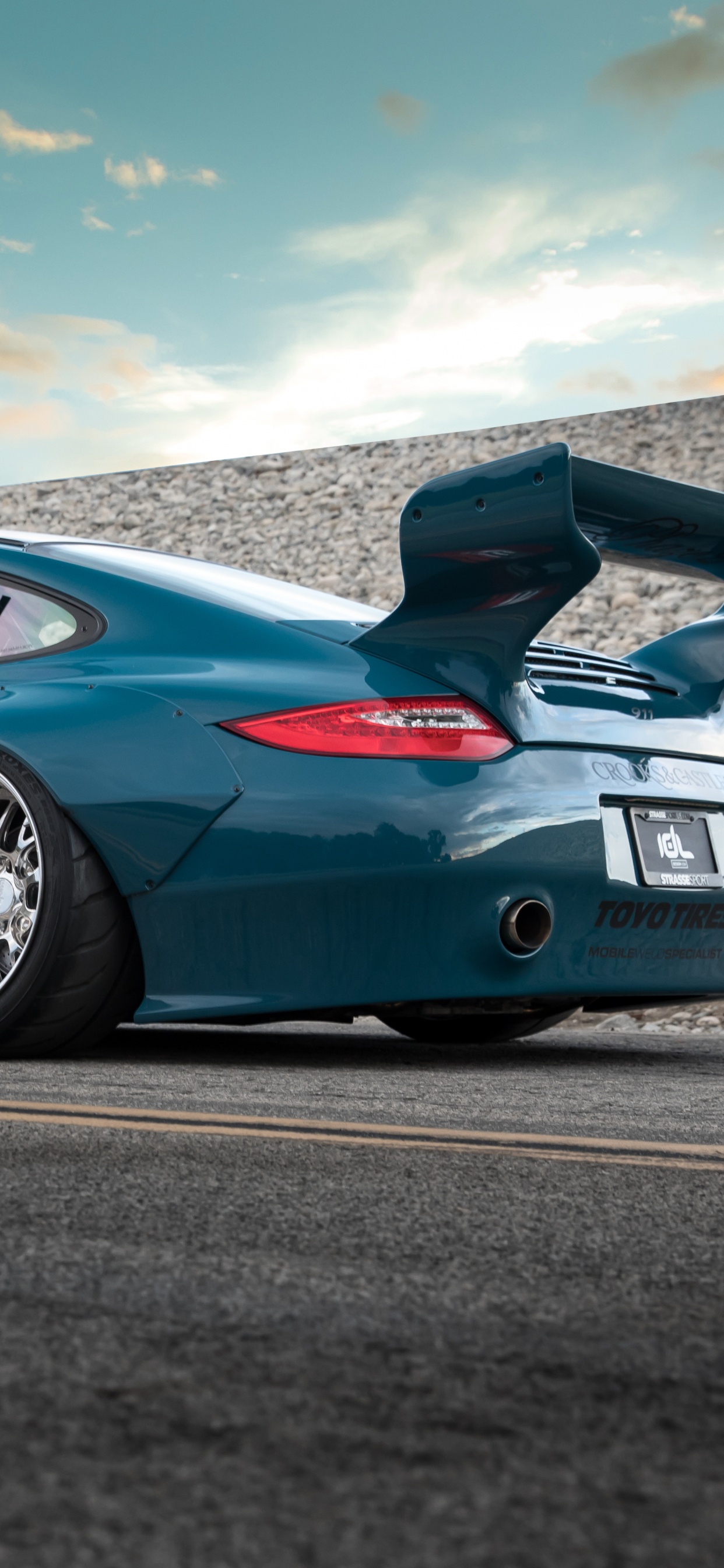 Porsche 911 Azul en la Carretera Bajo un Cielo Azul. Wallpaper in 1242x2688 Resolution