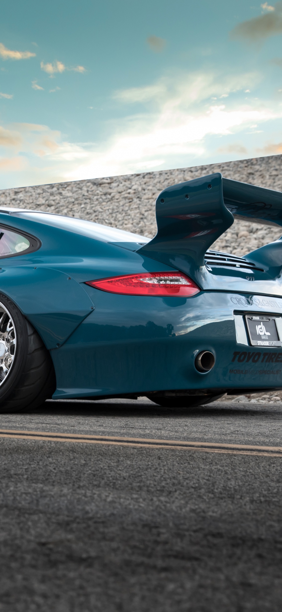 Porsche 911 Bleue Sur Route Sous Ciel Bleu. Wallpaper in 1125x2436 Resolution