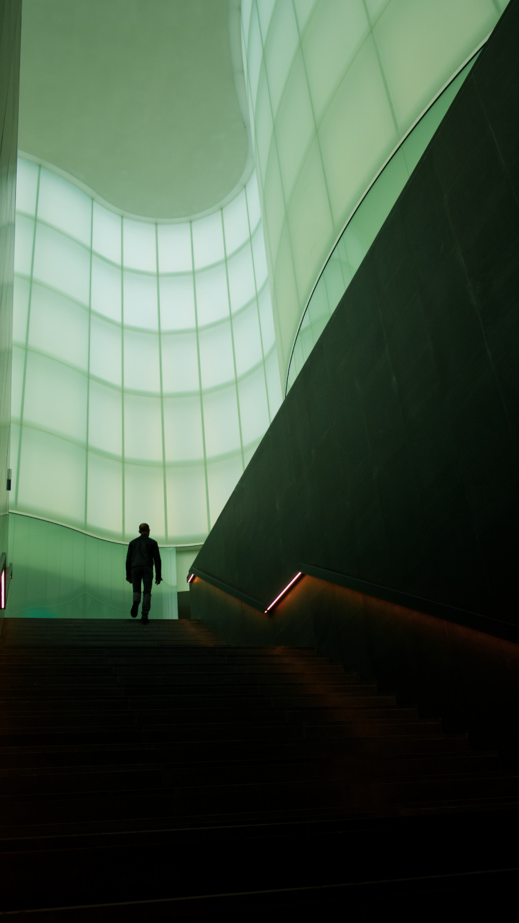 Man in Black Jacket Walking on Brown Staircase. Wallpaper in 750x1334 Resolution