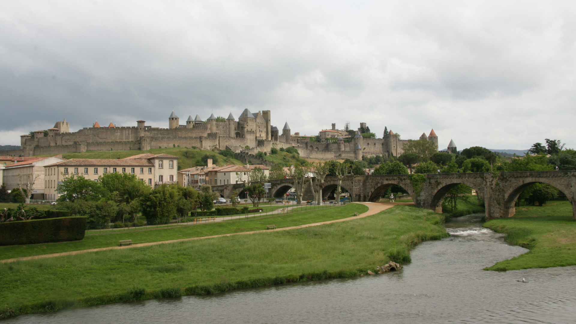 Bâtiment en Béton Brun Près du Champ D'herbe Verte et de la Rivière Sous Des Nuages Blancs Pendant la Journée. Wallpaper in 1920x1080 Resolution