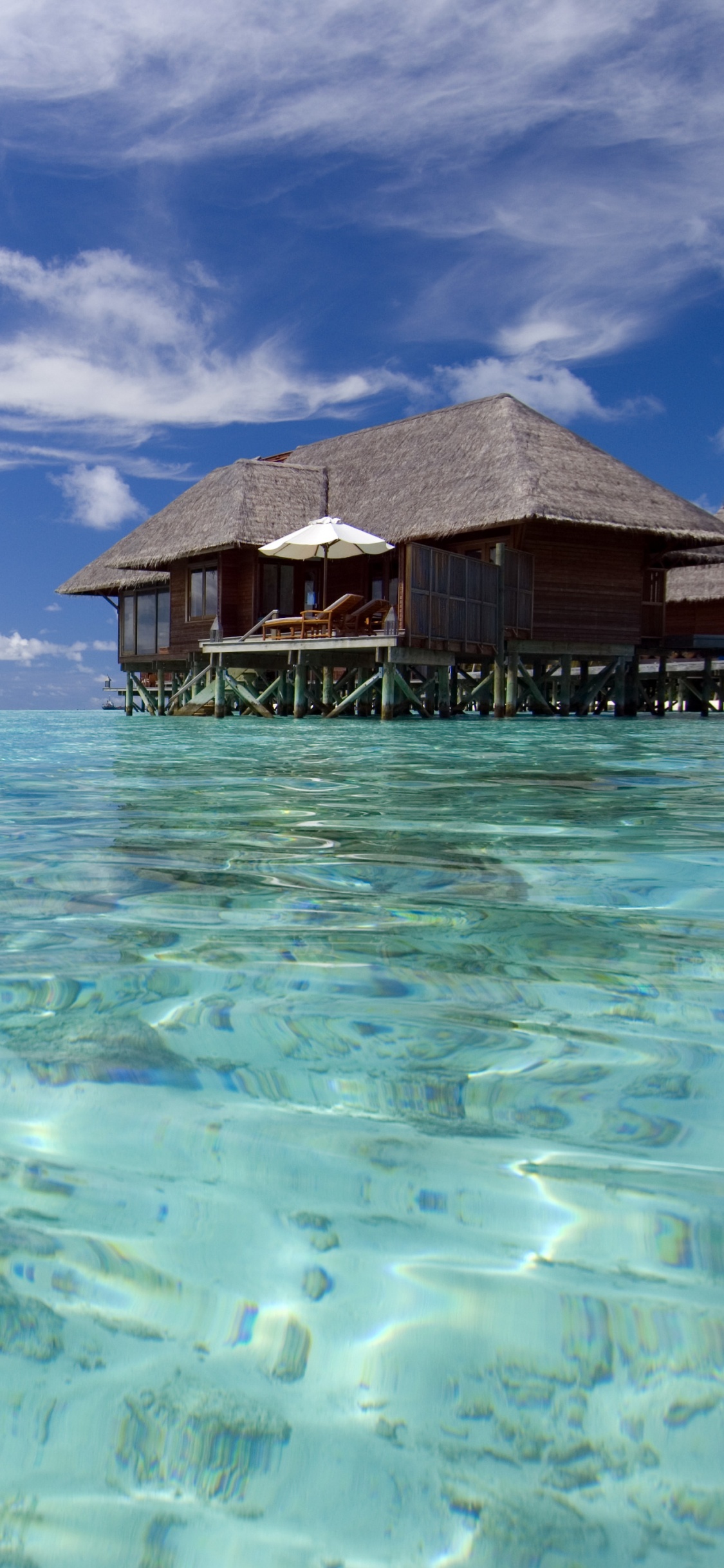 Casa de Madera Marrón Sobre el Cuerpo de Agua Bajo un Cielo Azul y Nubes Blancas Durante el Día. Wallpaper in 1125x2436 Resolution