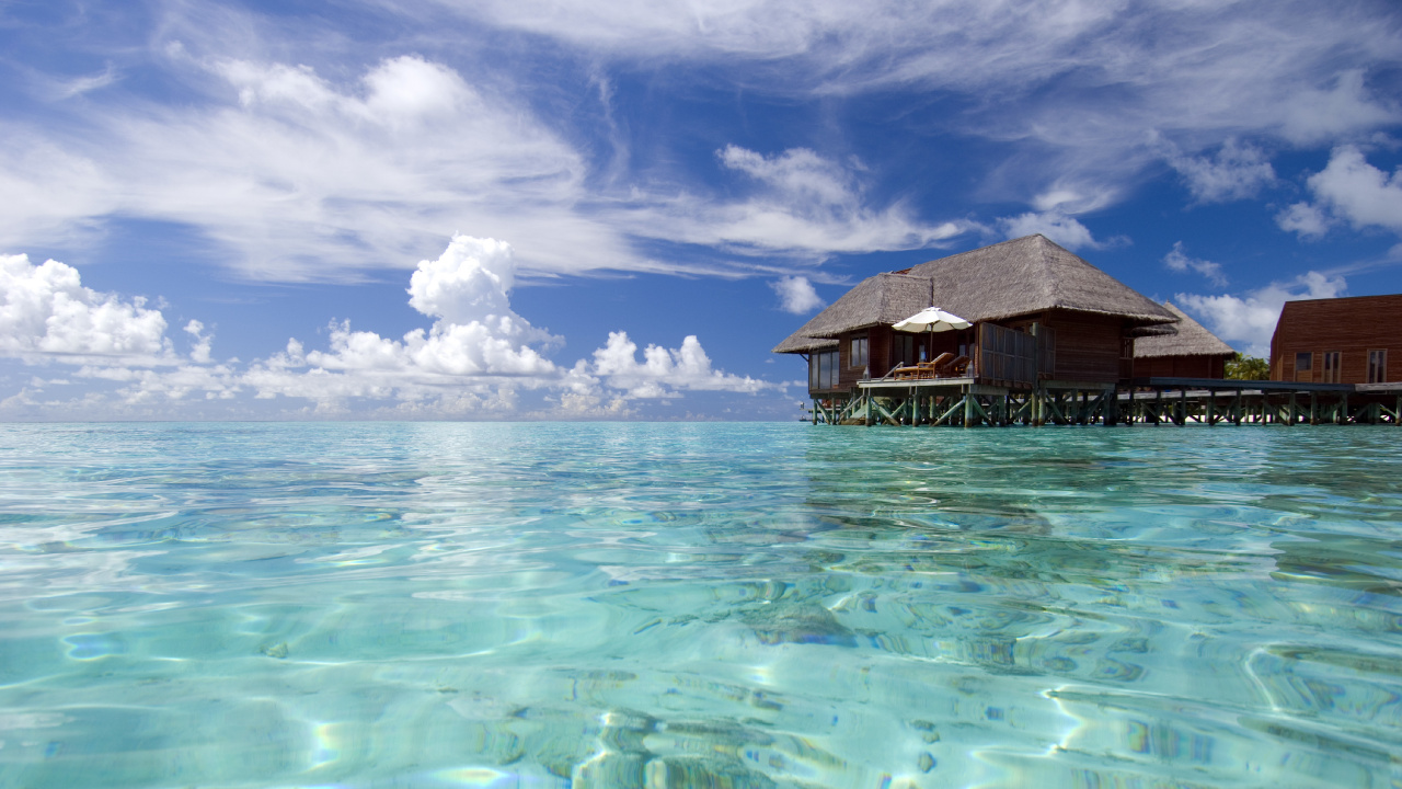 Casa de Madera Marrón Sobre el Cuerpo de Agua Bajo un Cielo Azul y Nubes Blancas Durante el Día. Wallpaper in 1280x720 Resolution