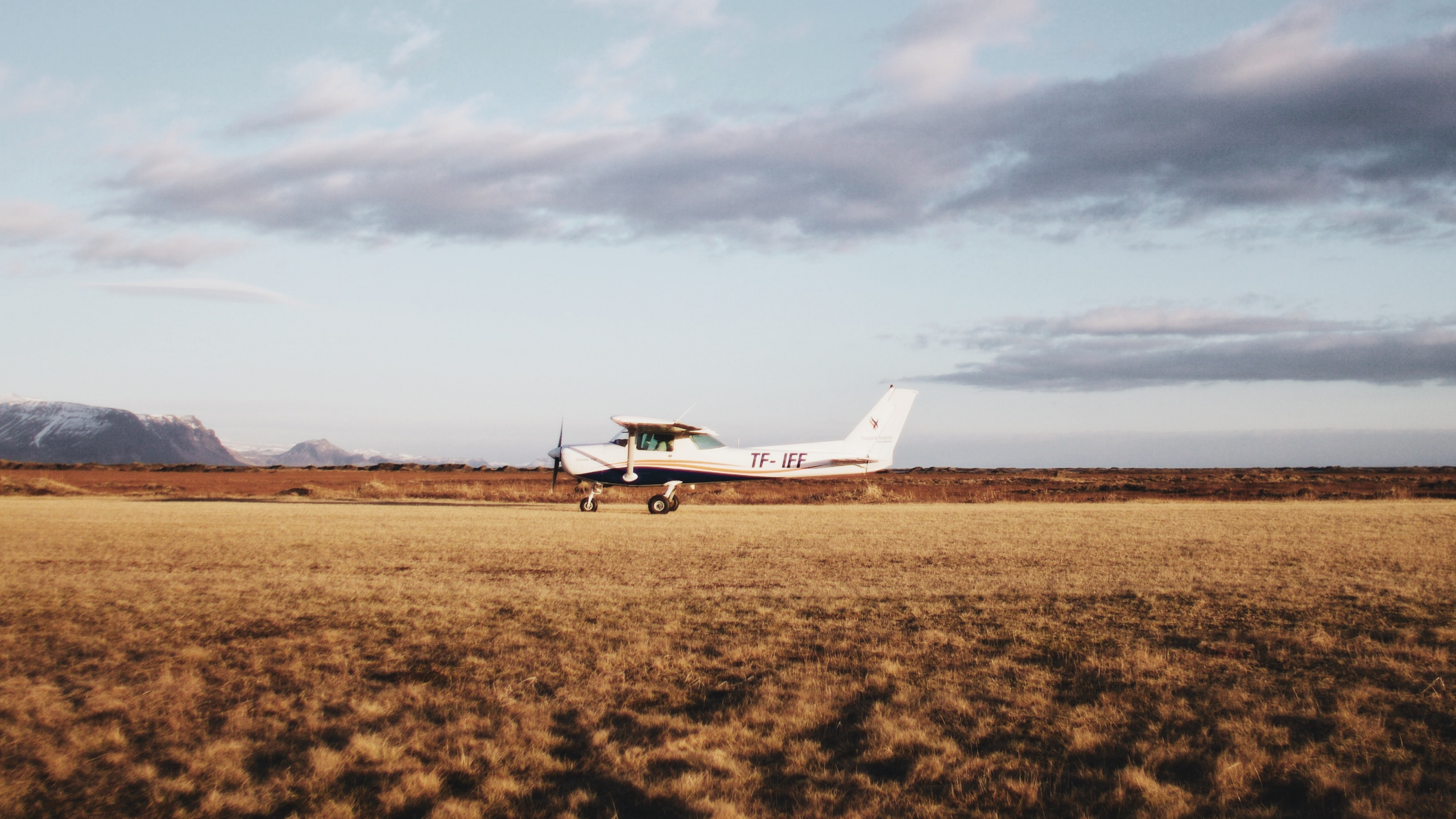 Avion Blanc Sur Champ Brun Sous Des Nuages Blancs Pendant la Journée. Wallpaper in 2560x1440 Resolution