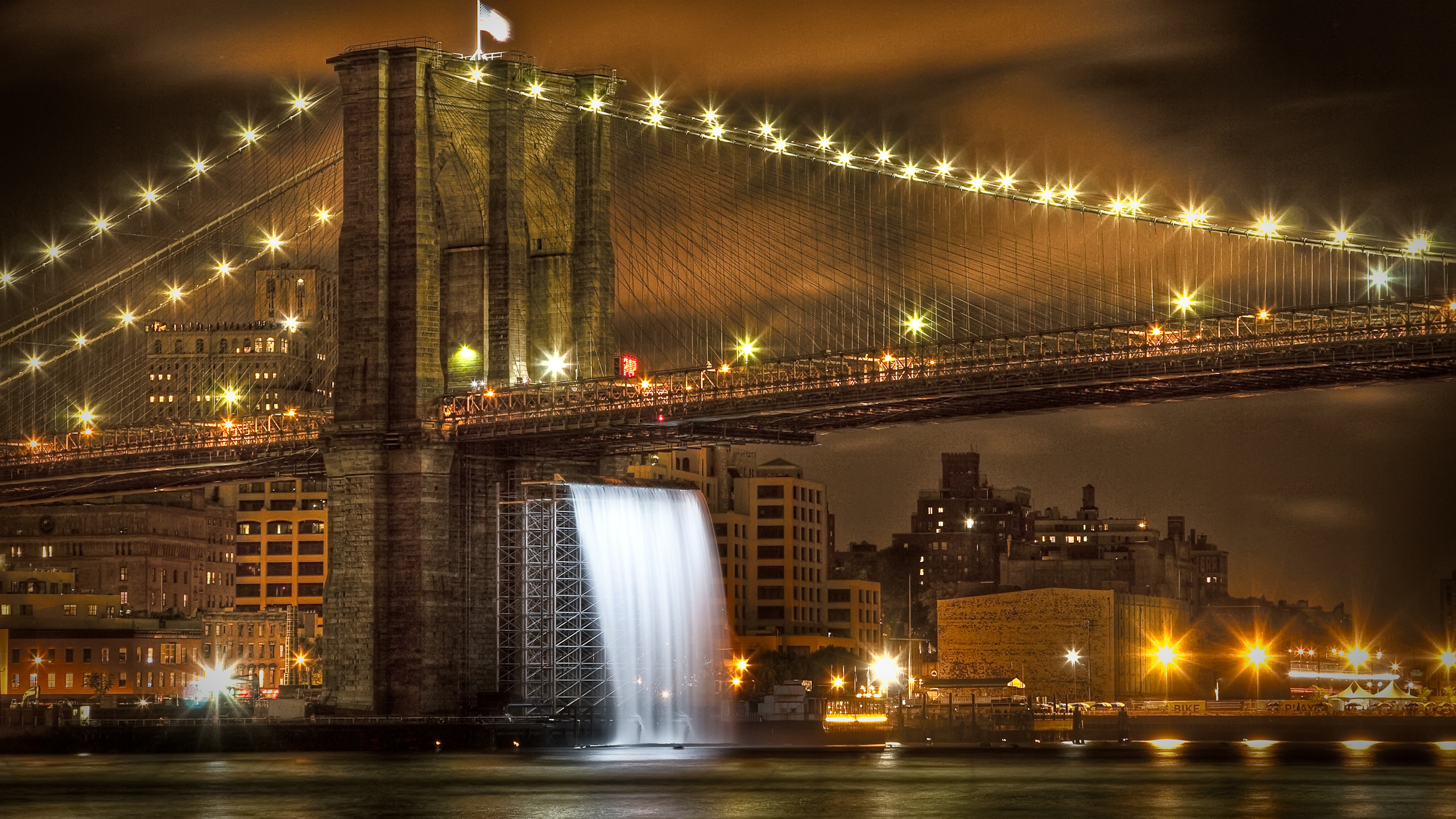 Puente Iluminado Cerca de Los Edificios de la Ciudad Durante la Noche.. Wallpaper in 2560x1440 Resolution