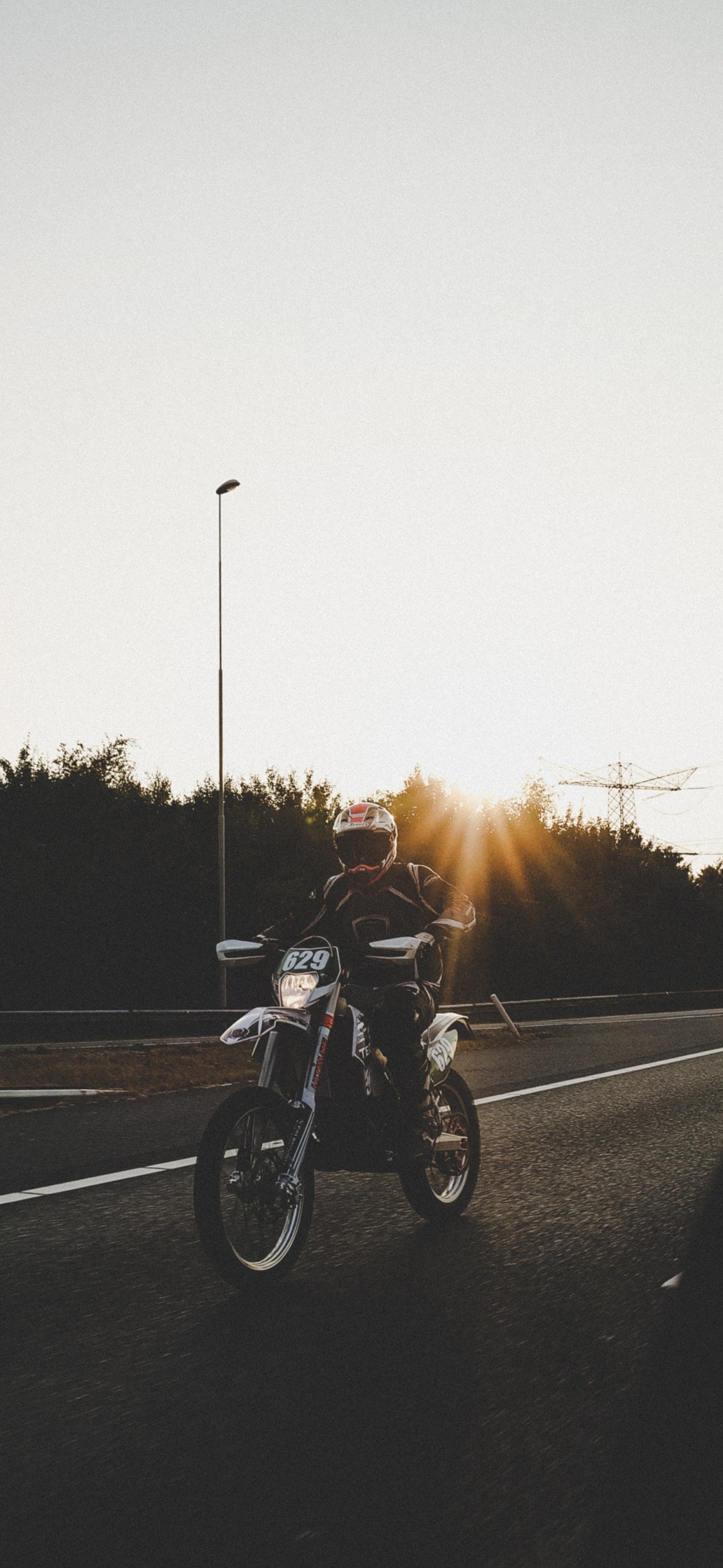 Hombre en Motocicleta en la Carretera Durante la Puesta de Sol. Wallpaper in 1125x2436 Resolution