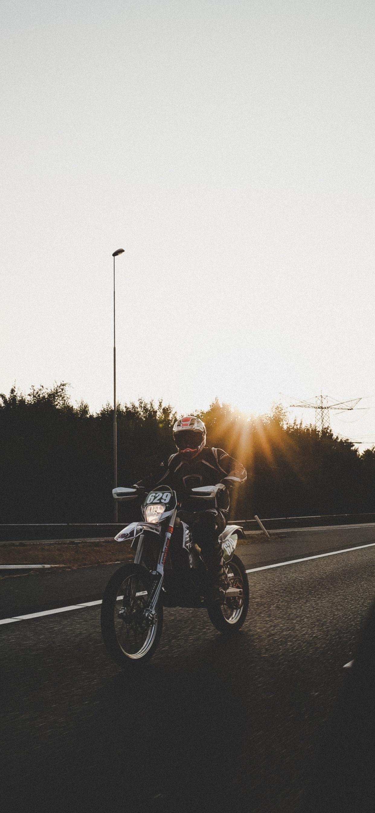 Hombre en Motocicleta en la Carretera Durante la Puesta de Sol. Wallpaper in 1242x2688 Resolution
