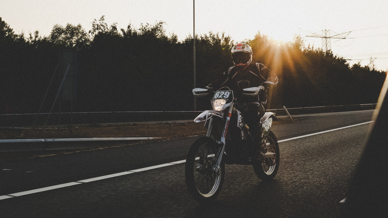 Mann, Der Während Des Sonnenuntergangs Motorrad Auf Der Straße Fährt. Wallpaper in 1280x720 Resolution