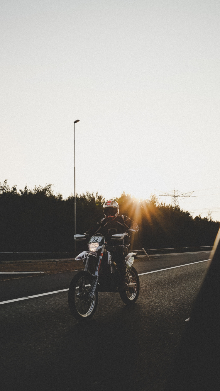 Man Riding Motorcycle Sur Route Pendant le Coucher du Soleil. Wallpaper in 750x1334 Resolution