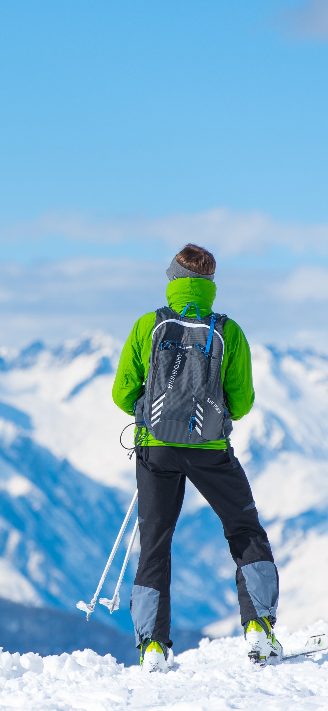 Hombre de Chaqueta Verde y Pantalón Negro de Pie Sobre un Suelo Cubierto de Nieve Durante el Día. Wallpaper in 1125x2436 Resolution