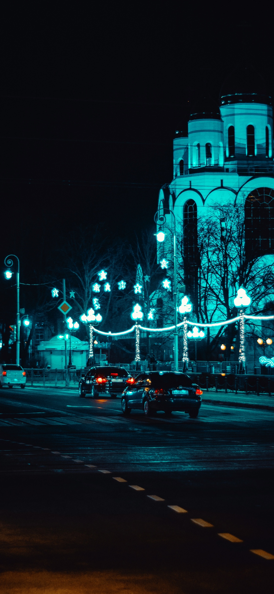 Voitures Sur Route Près D'un Bâtiment Éclairé Pendant la Nuit. Wallpaper in 1125x2436 Resolution