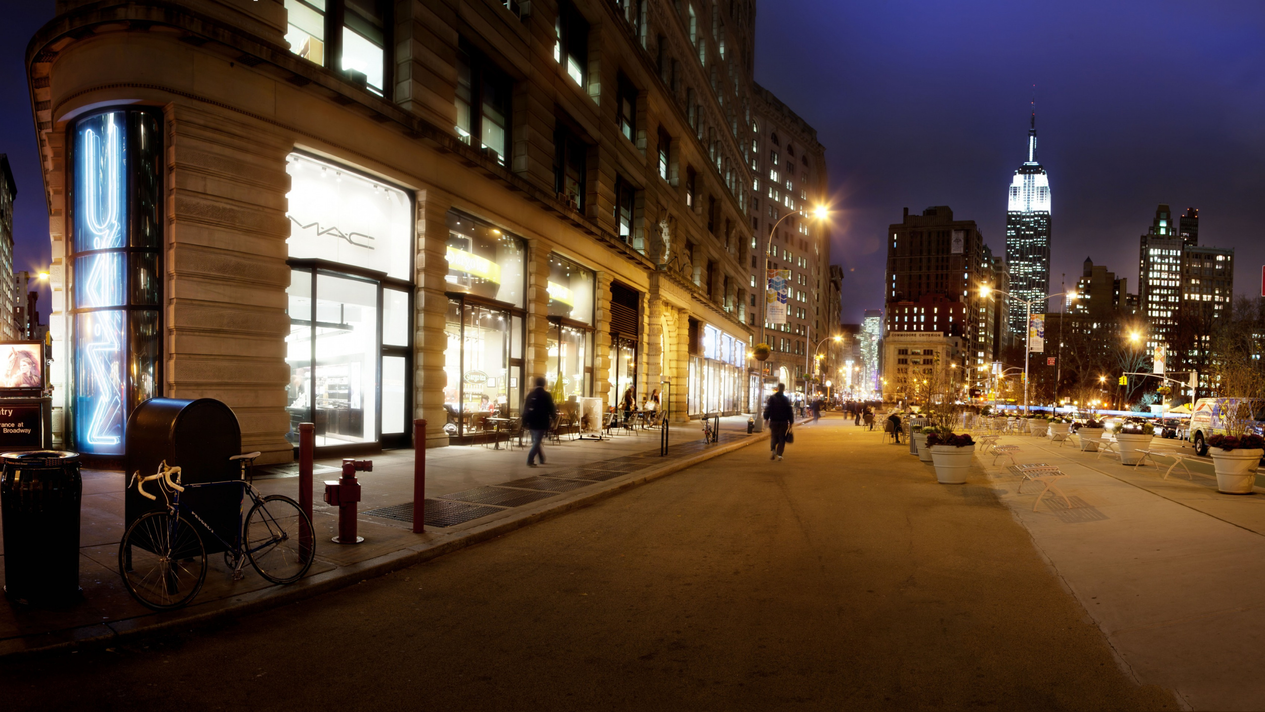 Gente Caminando en la Acera Cerca Del Edificio Durante la Noche. Wallpaper in 2560x1440 Resolution