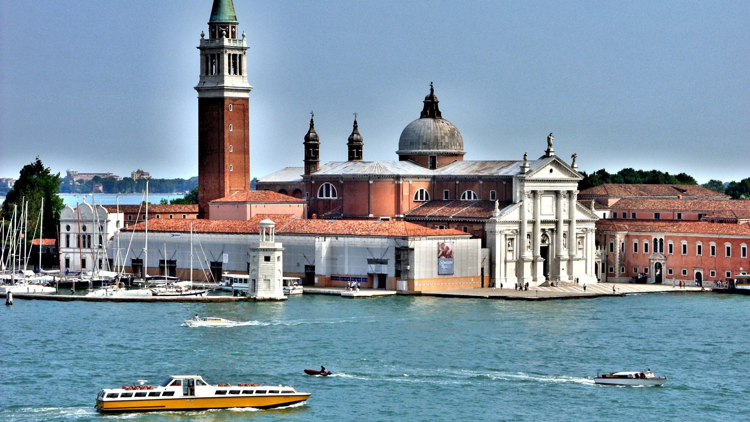 Brown and White Concrete Building Beside Body of Water During Daytime. Wallpaper in 2560x1440 Resolution
