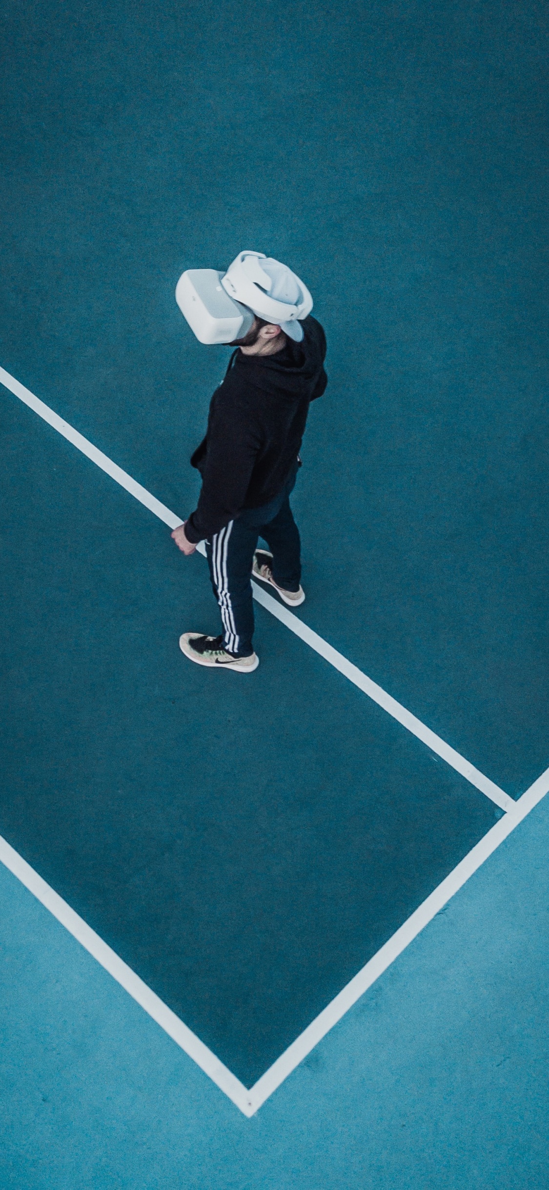 Person in Schwarzer Jacke Und Weißem Hut, Die Auf Grünem Boden Spielt. Wallpaper in 1125x2436 Resolution