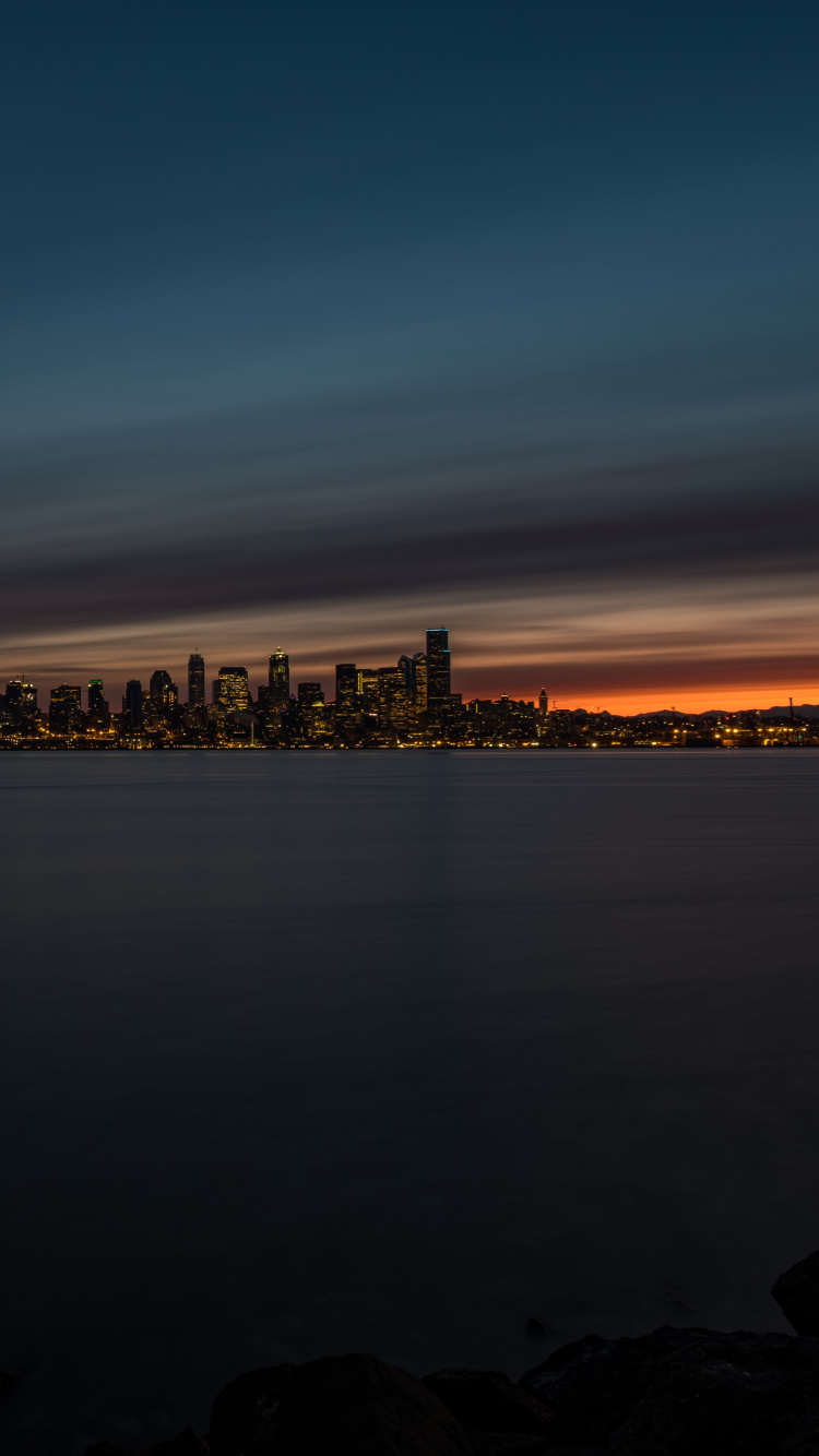 Skyline Der Stadt Über Gewässer Während Der Nacht. Wallpaper in 750x1334 Resolution