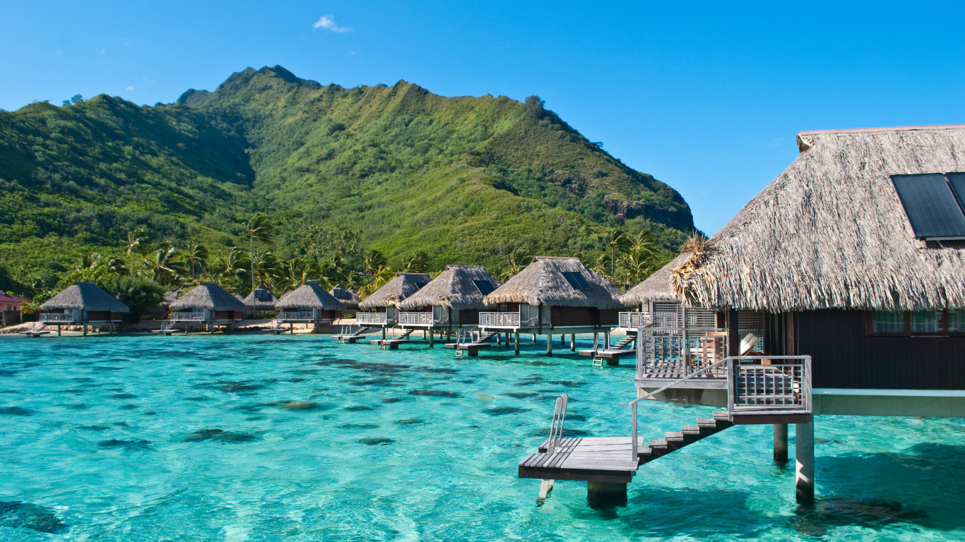 Brown Wooden House on Green Mountain Beside Body of Water During Daytime. Wallpaper in 1366x768 Resolution