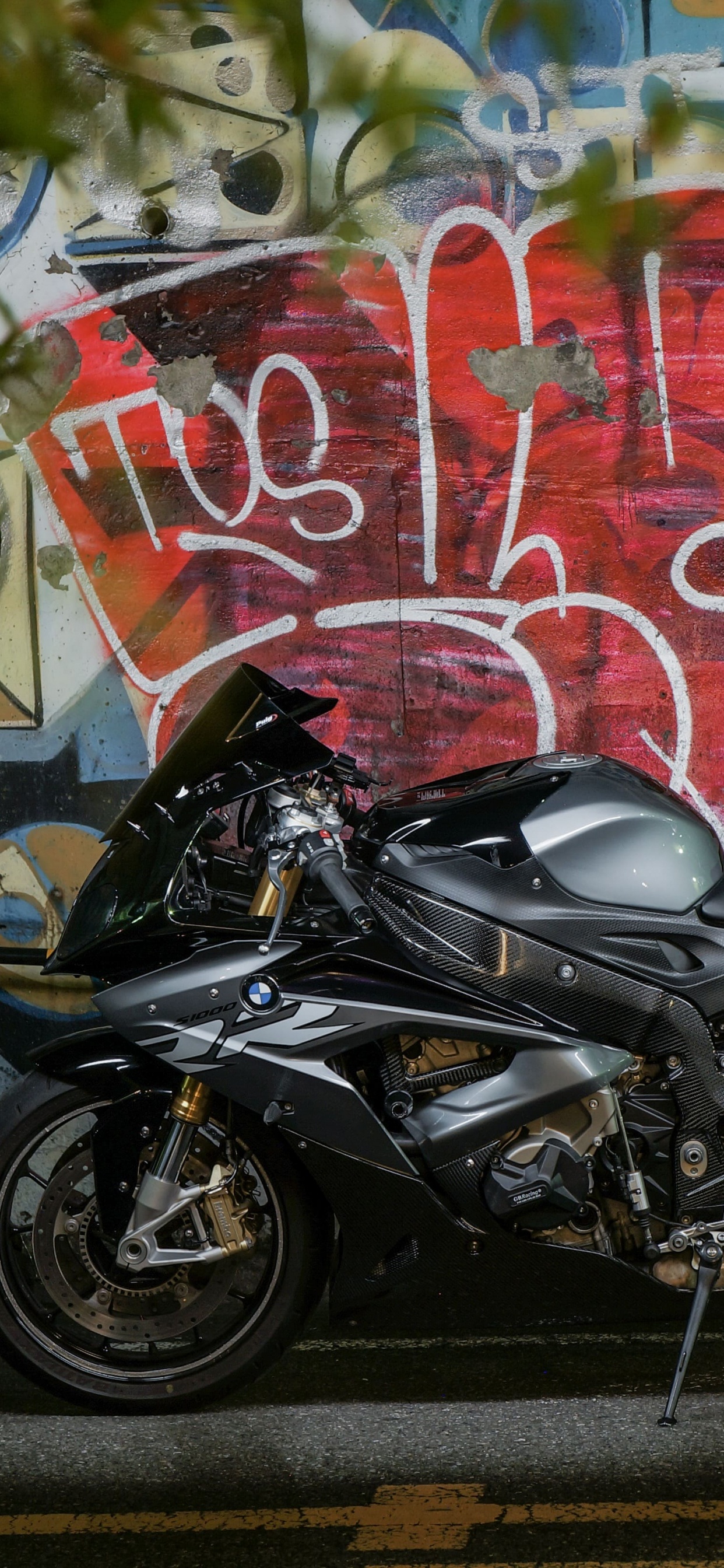 Black Motorcycle Parked Beside Wall With Graffiti. Wallpaper in 1242x2688 Resolution