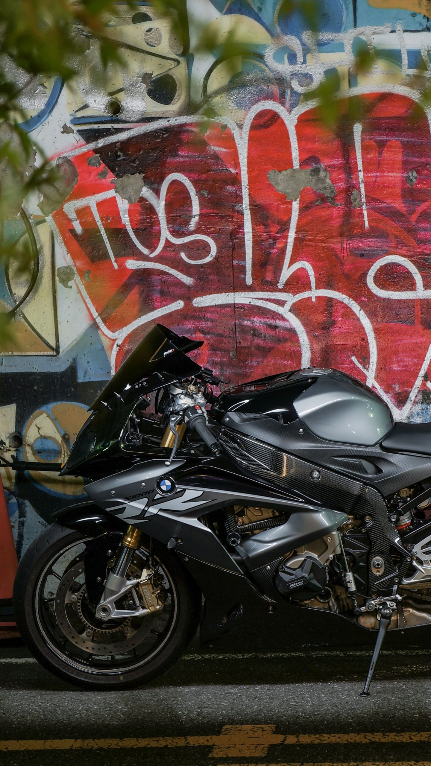 Black Motorcycle Parked Beside Wall With Graffiti. Wallpaper in 1440x2560 Resolution