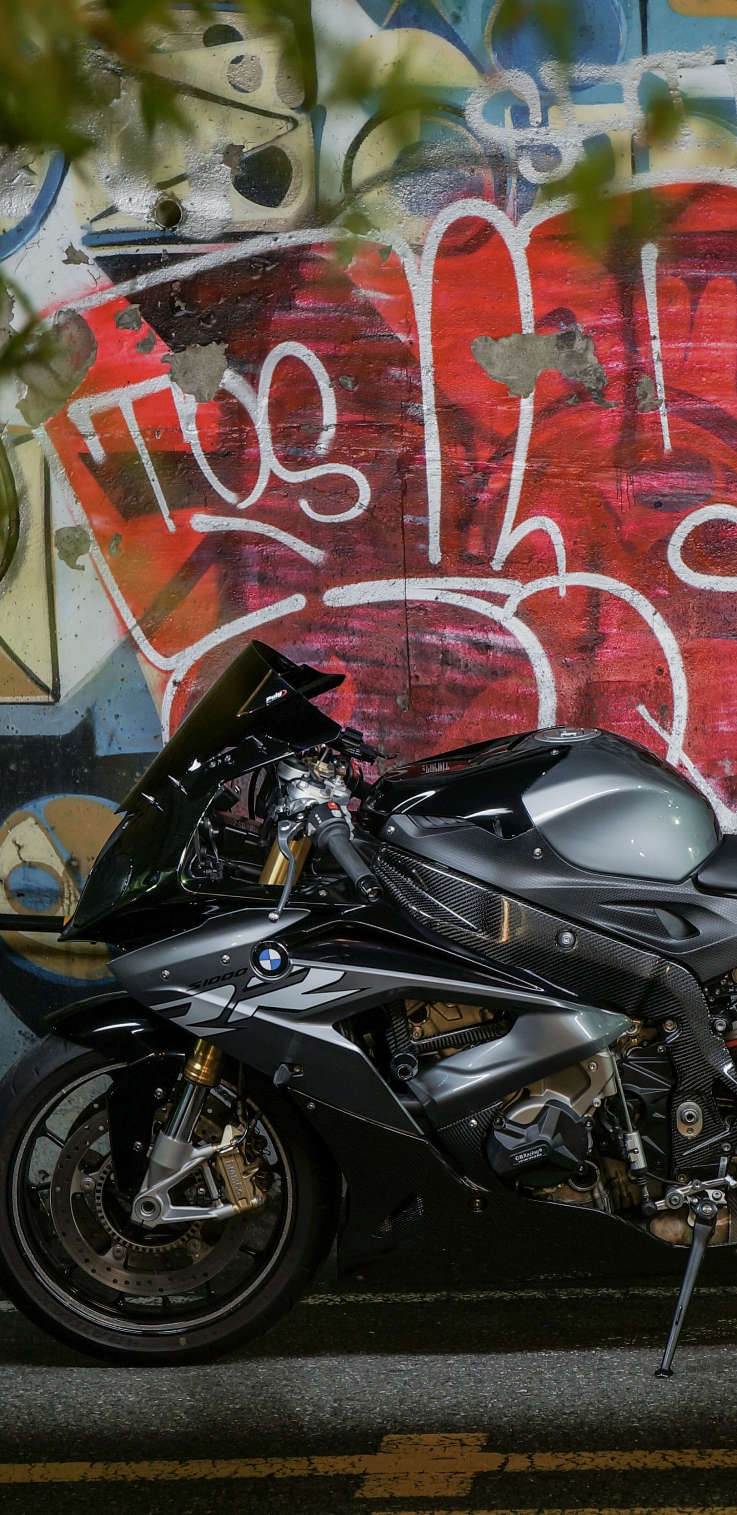 Black Motorcycle Parked Beside Wall With Graffiti. Wallpaper in 1440x2960 Resolution