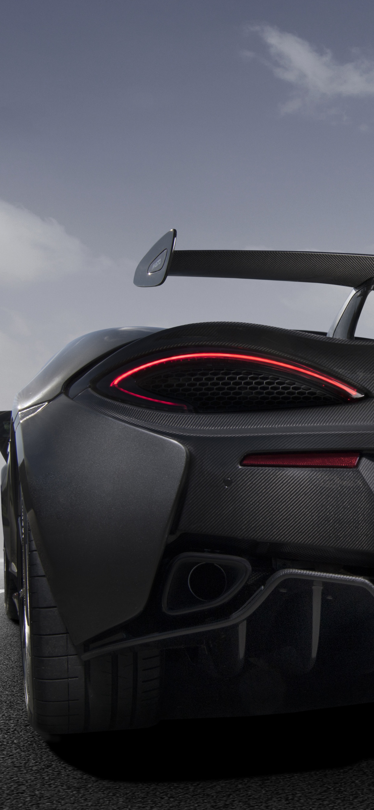 Black Porsche 911 on Gray Asphalt Road Under Gray Cloudy Sky. Wallpaper in 1242x2688 Resolution