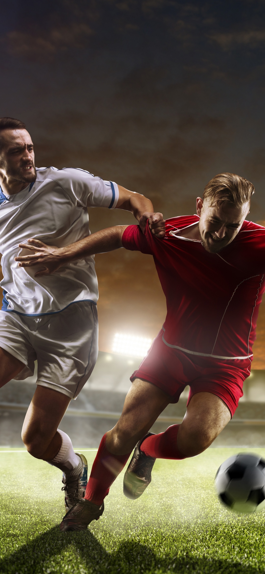 2 Männer Spielen Nachts Fußball Auf Grünem Rasen. Wallpaper in 1125x2436 Resolution