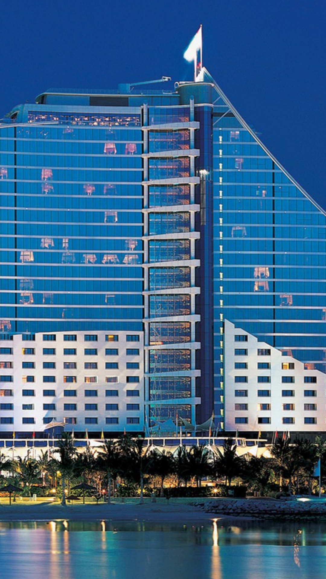 Blue and White Glass Building Near Body of Water During Night Time. Wallpaper in 1080x1920 Resolution