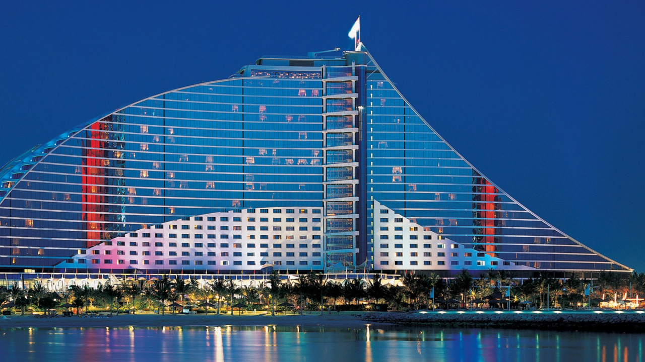 Blue and White Glass Building Near Body of Water During Night Time. Wallpaper in 1280x720 Resolution