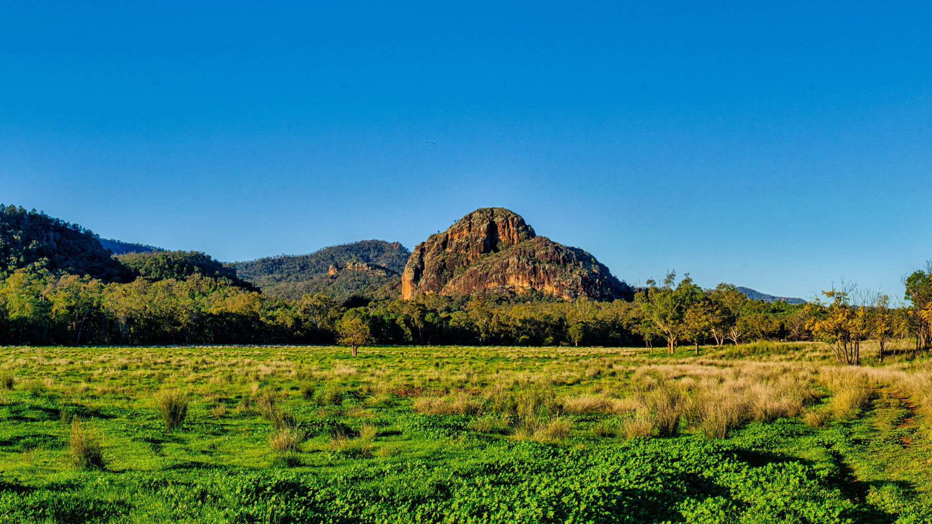 Green Grass Field Near Brown Mountain Under Blue Sky During Daytime. Wallpaper in 1920x1080 Resolution