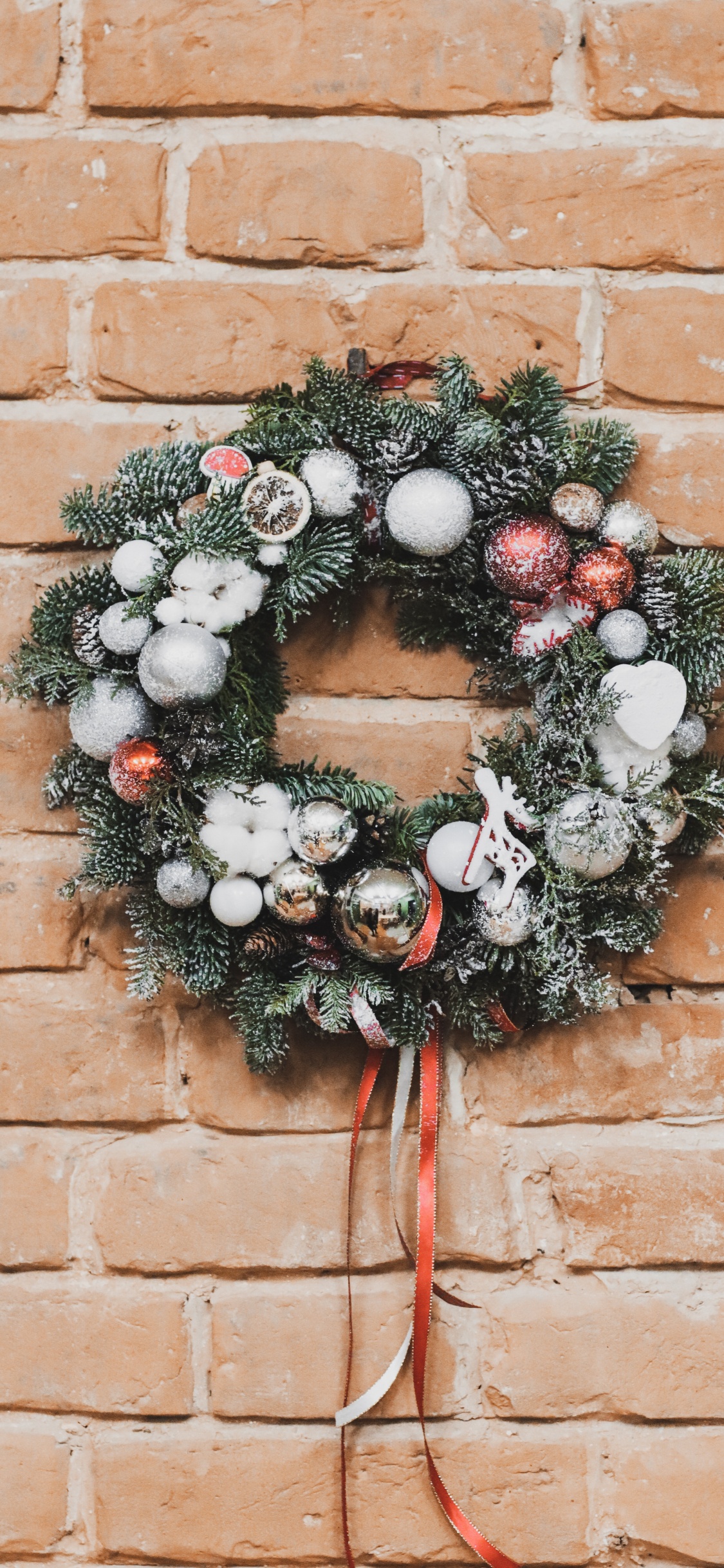Green and White Wreath on Brown Brick Wall. Wallpaper in 1125x2436 Resolution