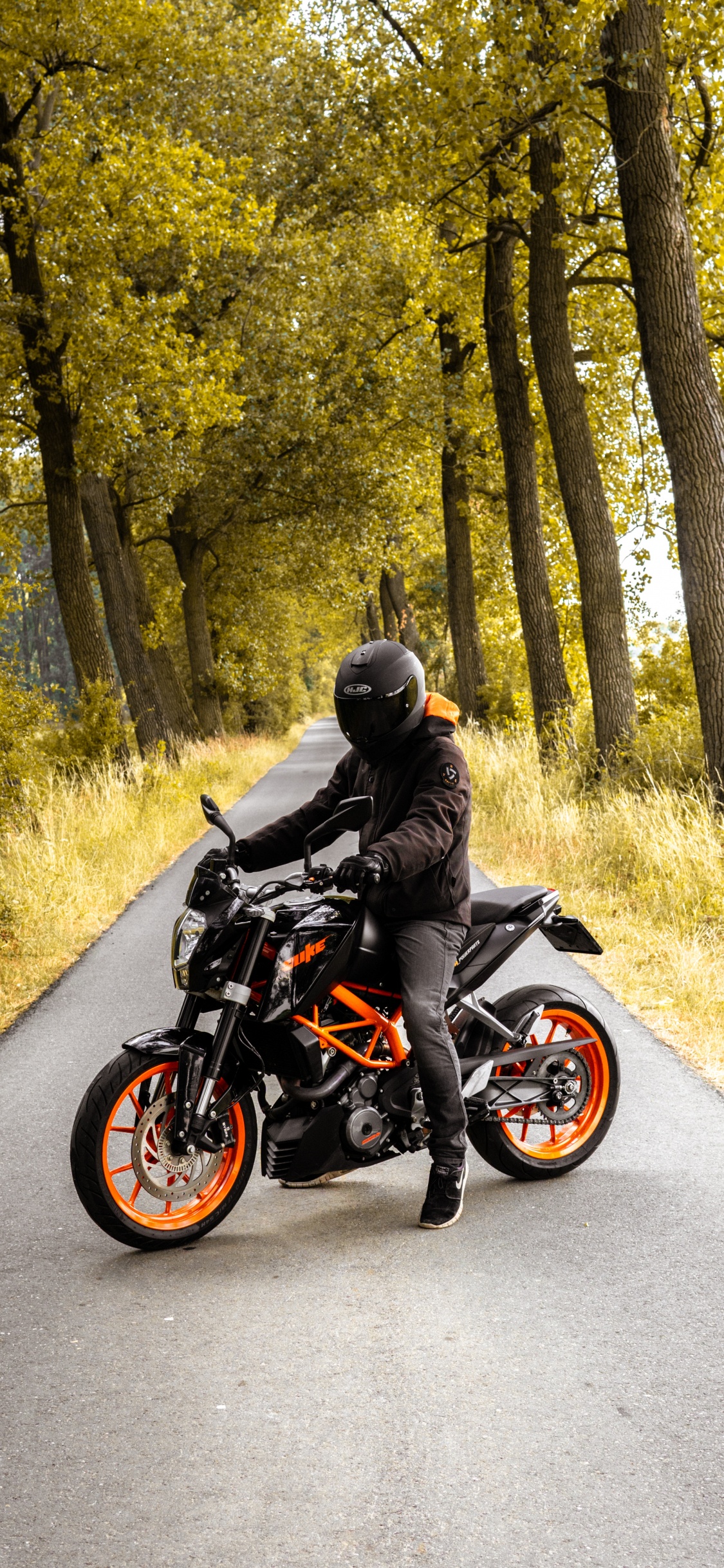 Hombre de Chaqueta Negra Montando Motocicleta Negra en la Carretera Durante el Día. Wallpaper in 1125x2436 Resolution