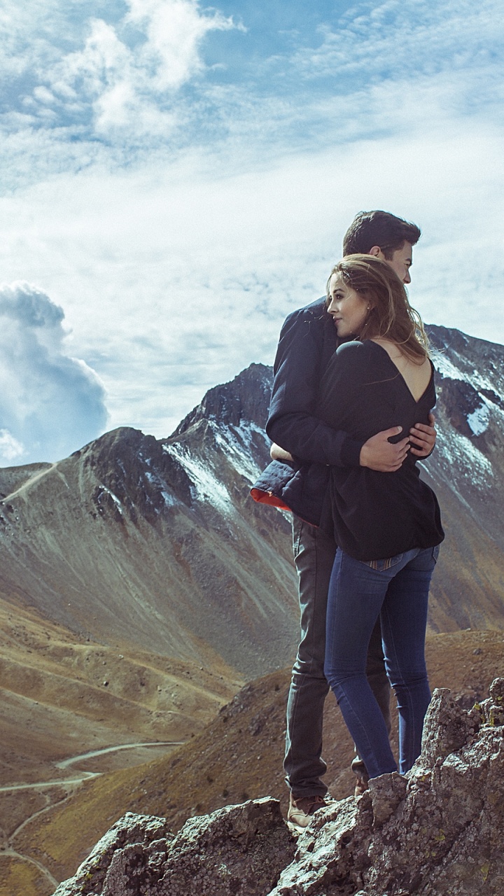 Hombre de Chaqueta Negra y Pantalón Negro de Pie Sobre la Formación Rocosa Bajo Las Nubes Blancas Durante el Día. Wallpaper in 720x1280 Resolution